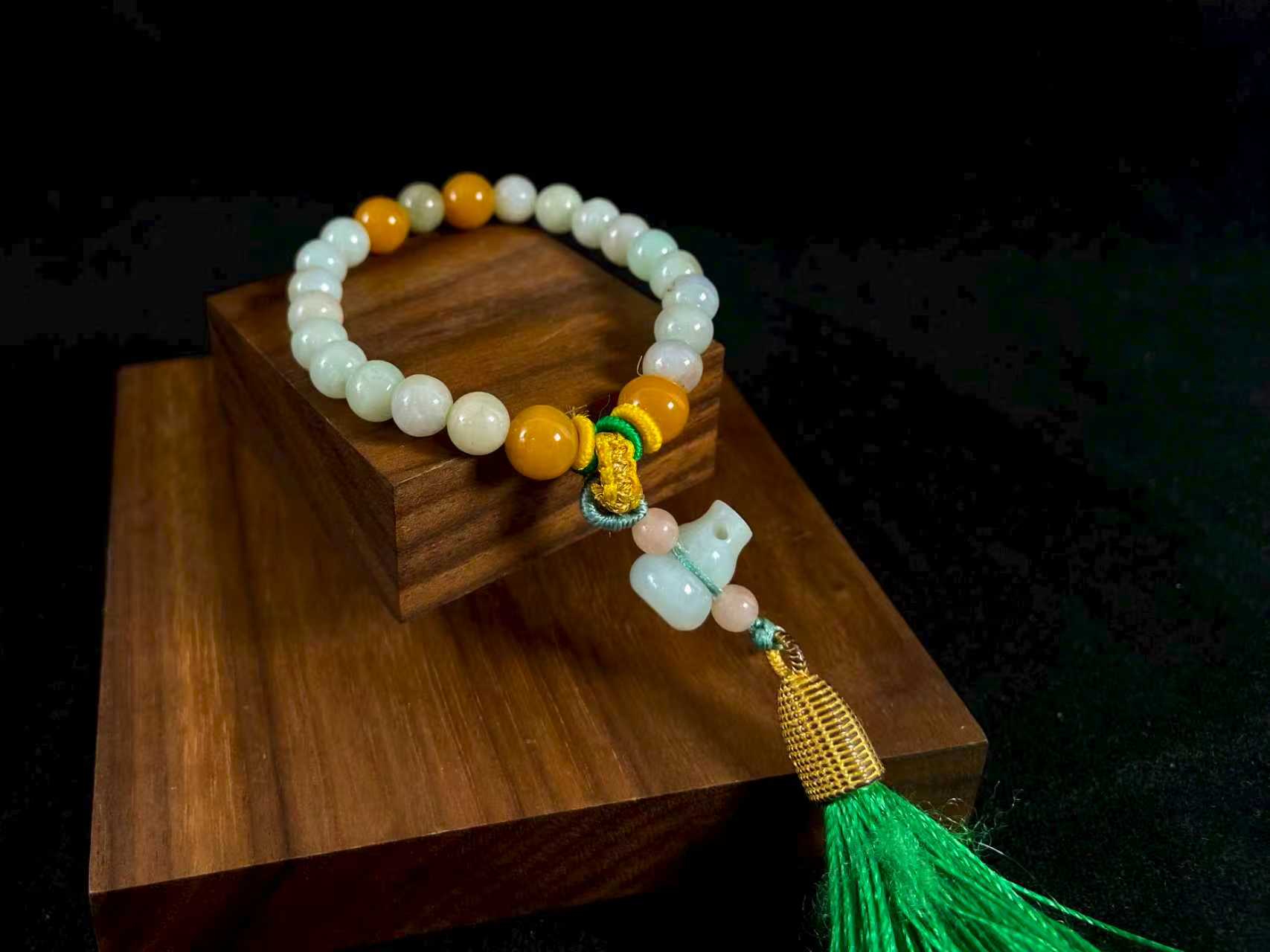 A milky white jade strand with gold, brown, and pink beads, gourd pendant, and green tassel.