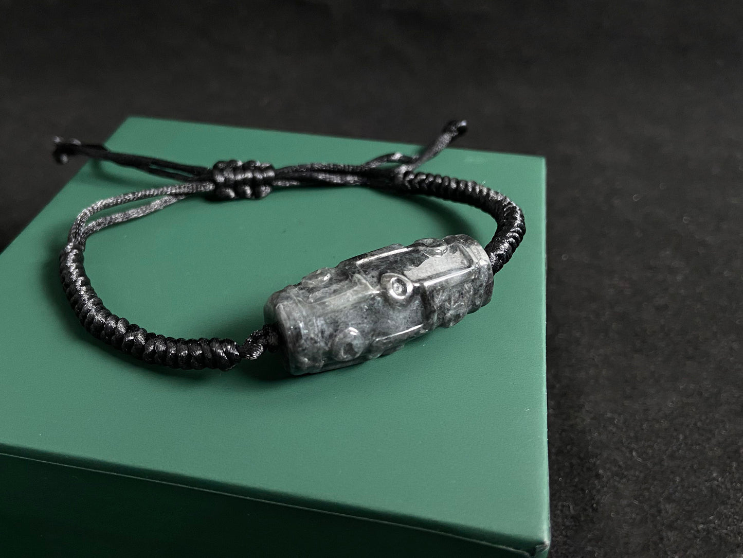 This braided bracelet combines a black cord with smooth gray "Lulutong" jade beads, creating a timeless and meaningful accessory.