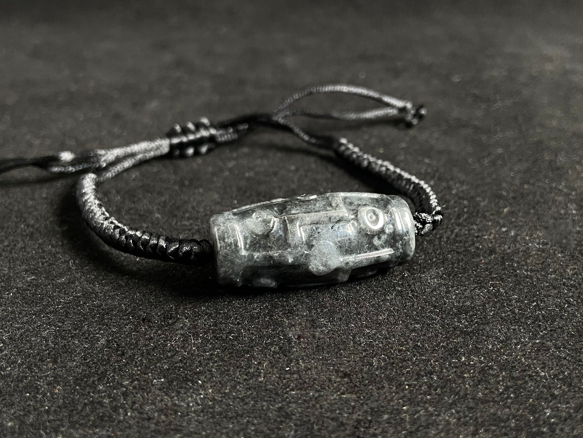 This braided bracelet combines a black cord with smooth gray "Lulutong" jade beads, creating a timeless and meaningful accessory.