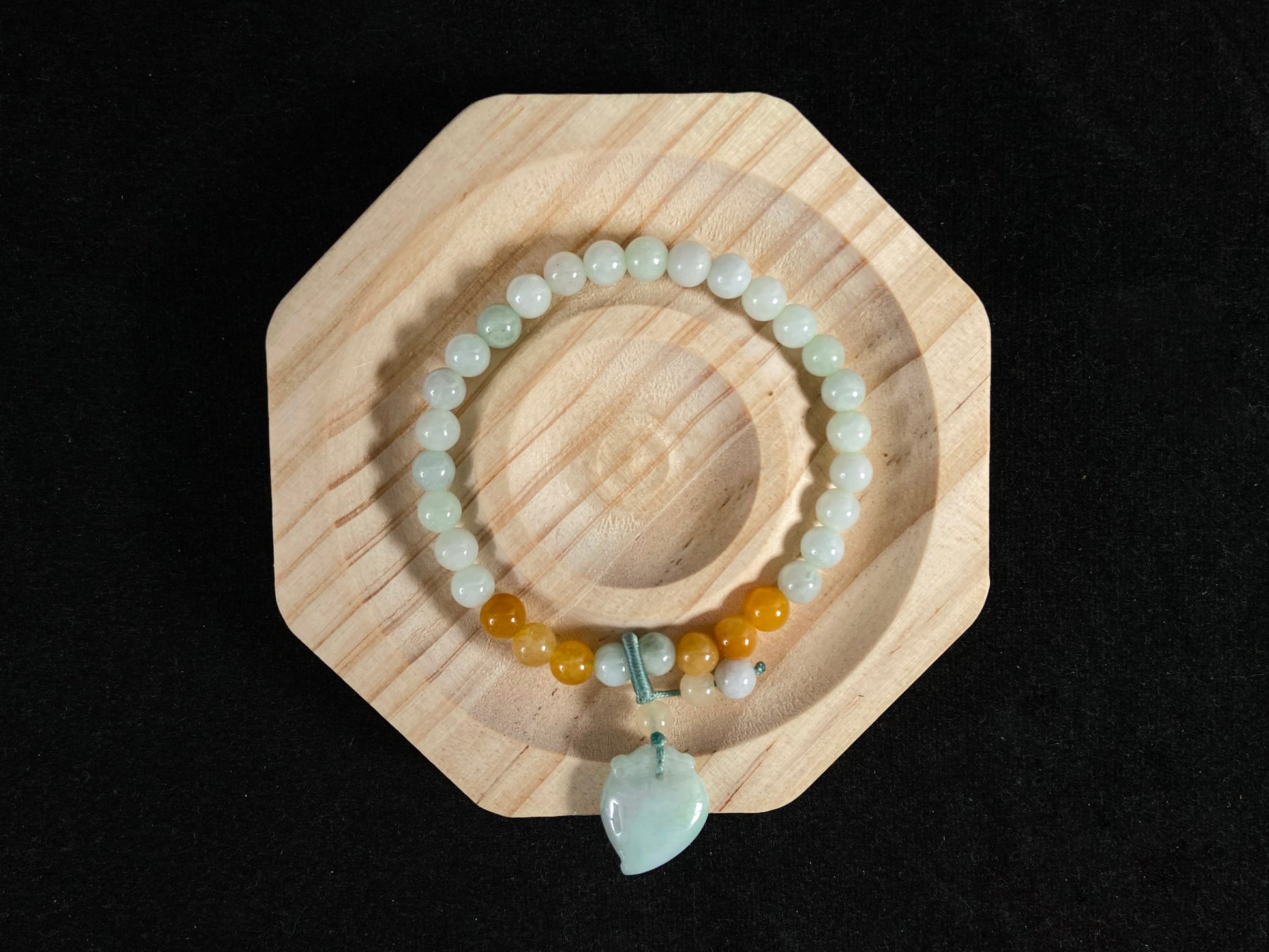 A jade bead strand with a white green peach pendant and tan/white green beads.