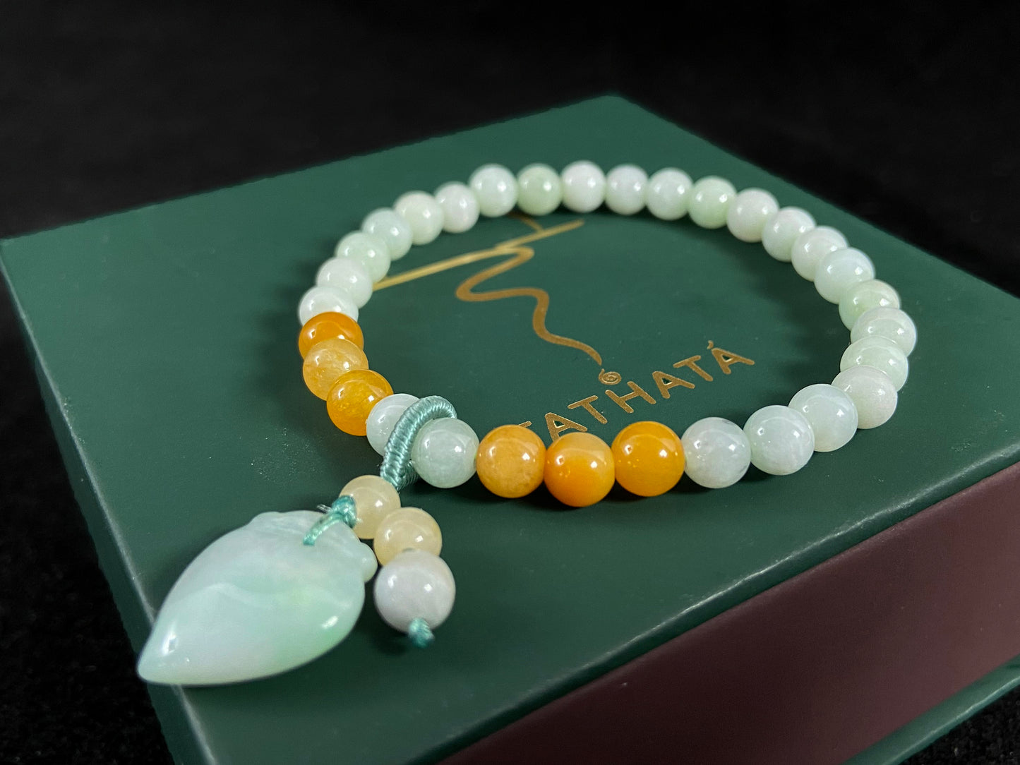 A jade bead strand with a white green peach pendant and tan/white green beads.