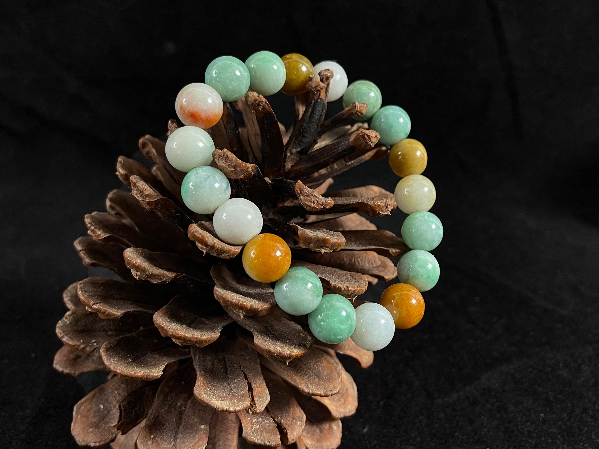 A jade bead strand predominantly green with brown, gold, and white accents.