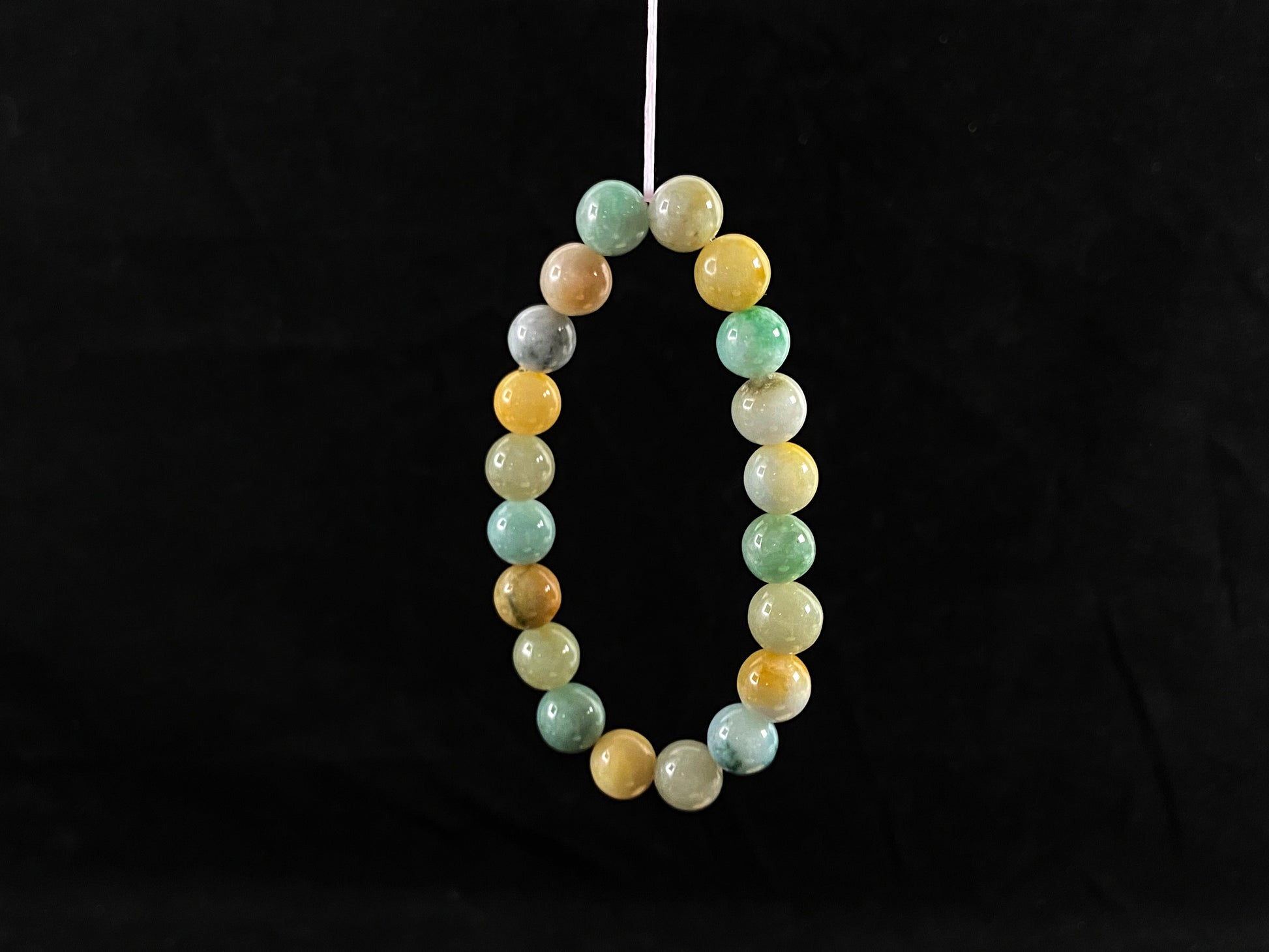 A strand of uniform jade beads in seafoam green, brown, yellow, light yellow green, forest green and lavender white.