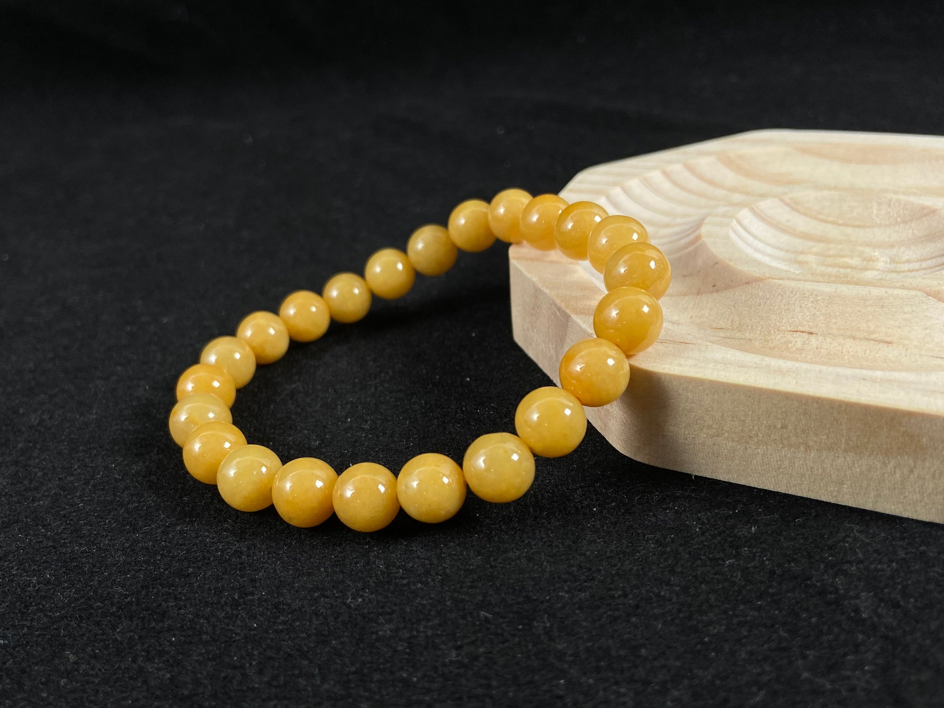 Yellow beaded bracelet on a dark surface with a wooden box in the background