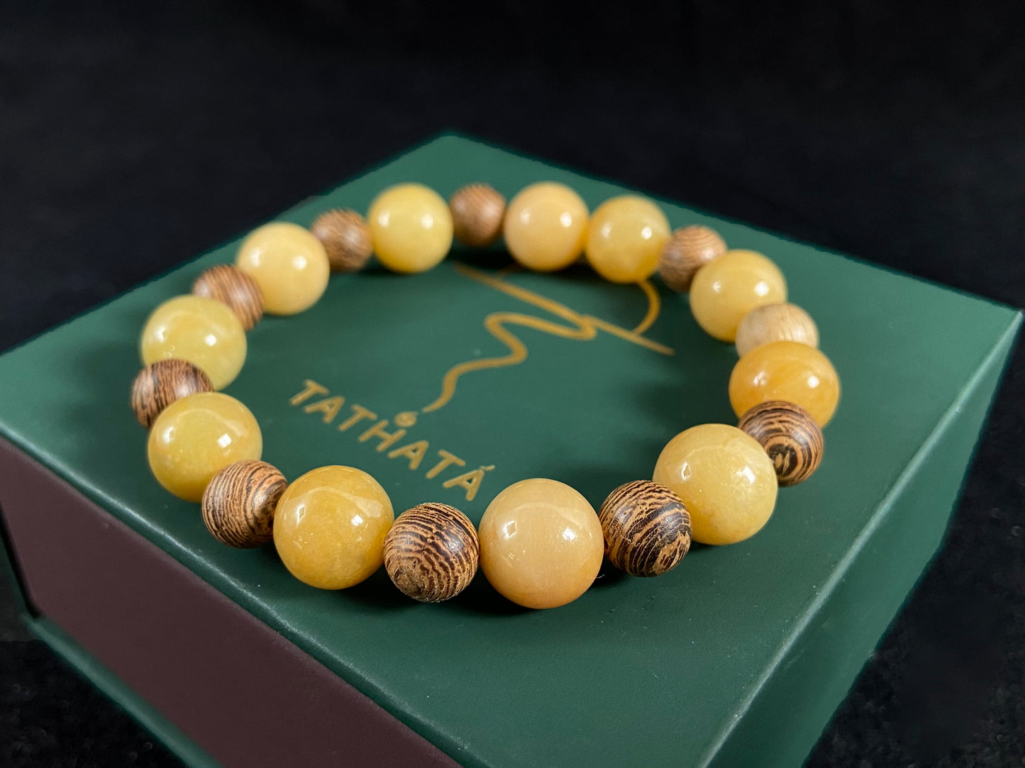 Beaded bracelet with yellow and brown beads on a green box with 'TATHATA' branding.
