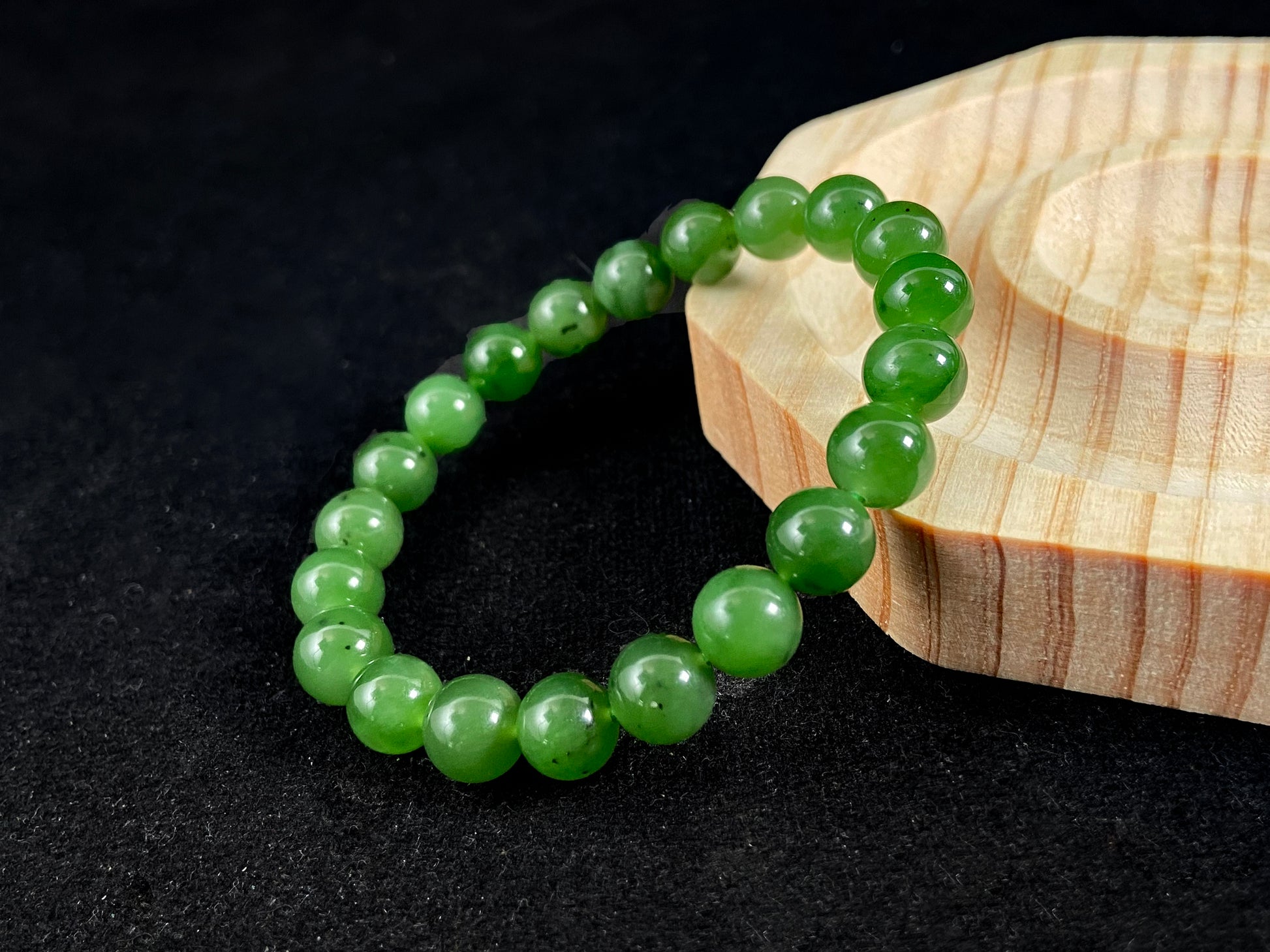 A yang green jade bead strand with subtle black speckling.