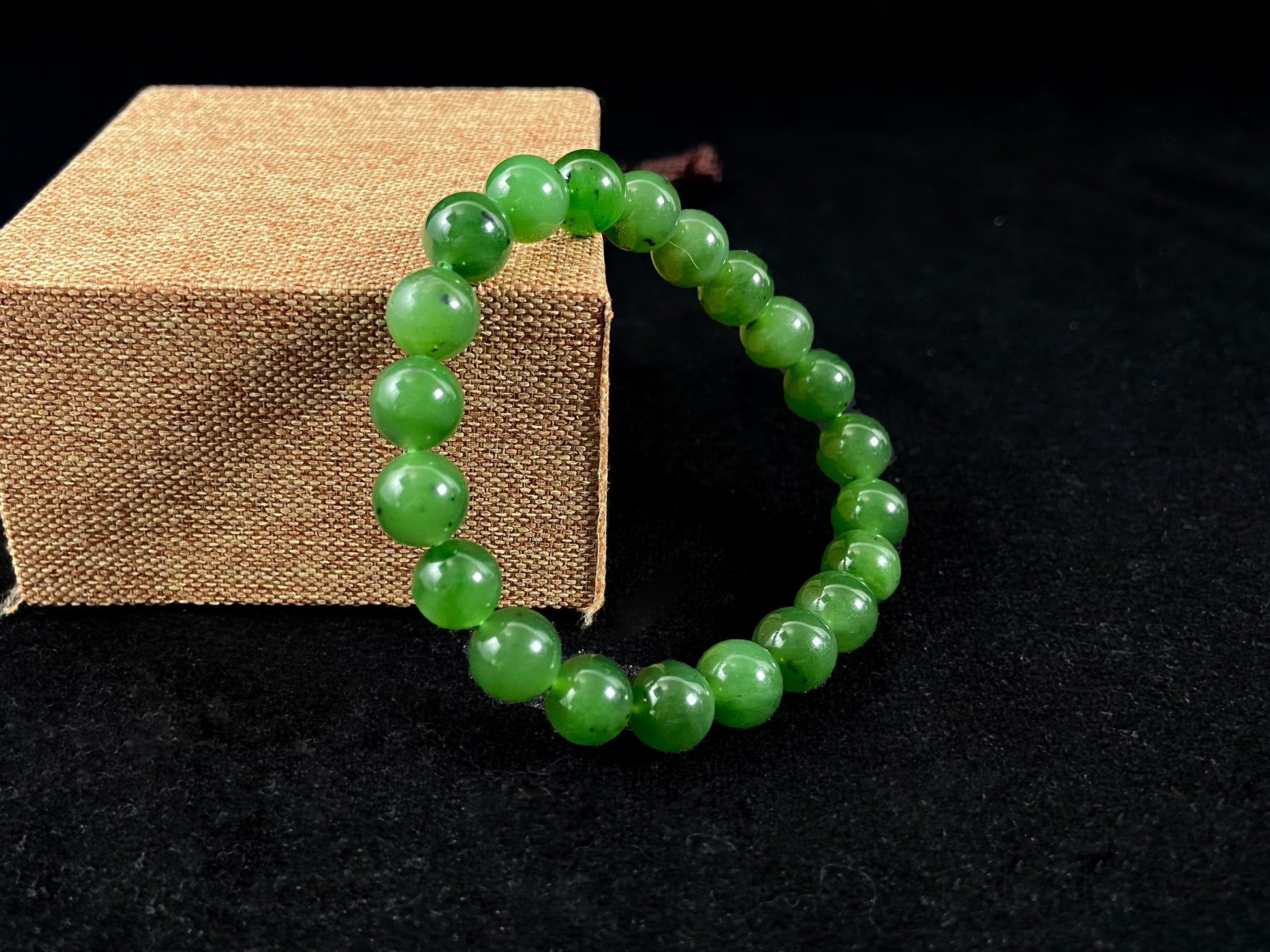 A yang green jade bead strand with subtle black speckling.