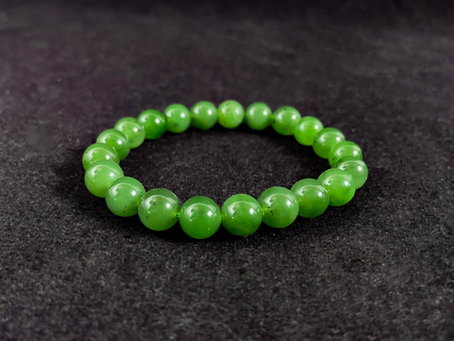 A yang green jade bead strand with subtle black speckling.