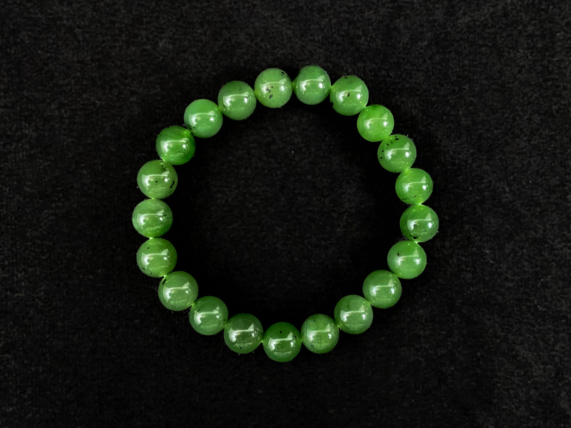 A yang green jade bead strand with subtle black speckling.