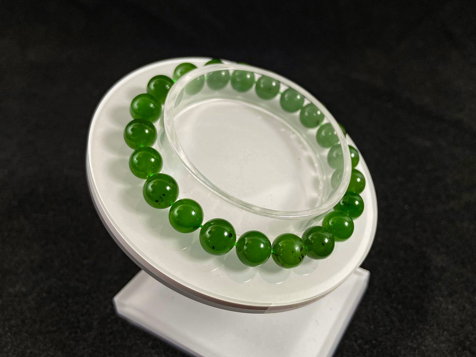A yang green jade bead strand with subtle black speckling.