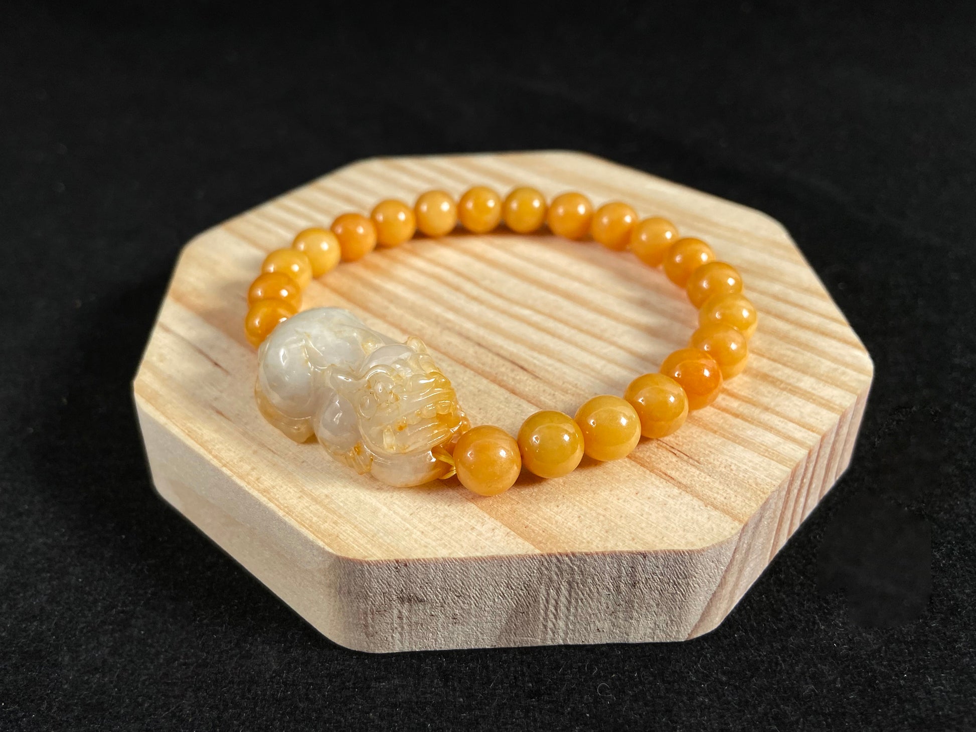 A jade bead strand featuring a white based gold flecked pixiu charm and yellow beads.