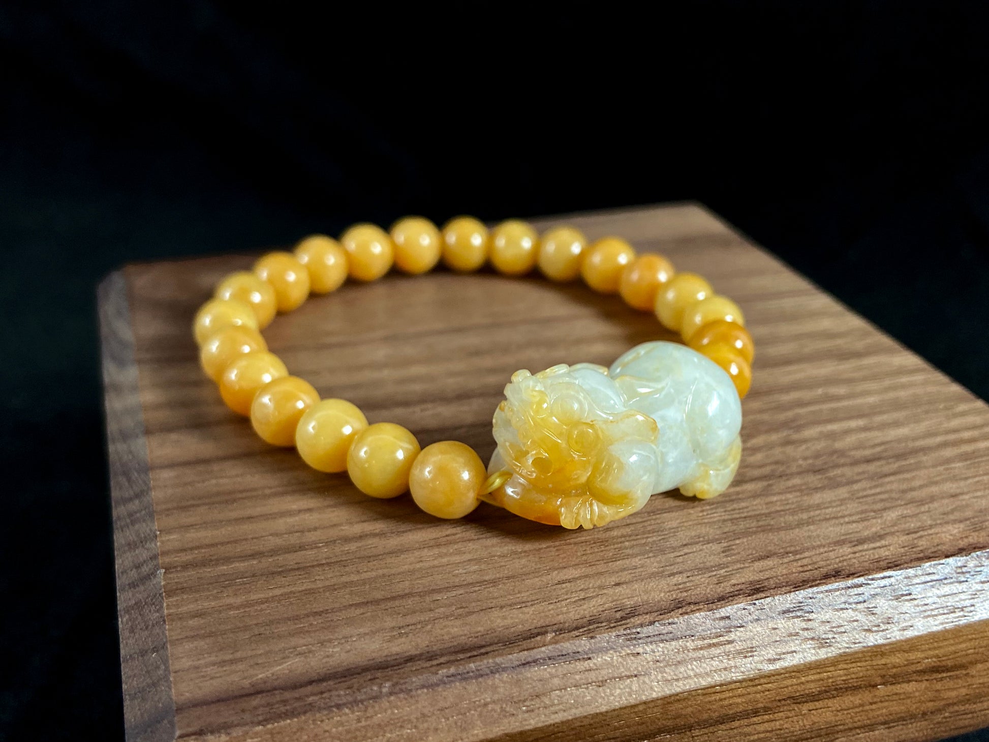 A jade bead strand featuring a white based gold flecked pixiu charm and yellow beads.