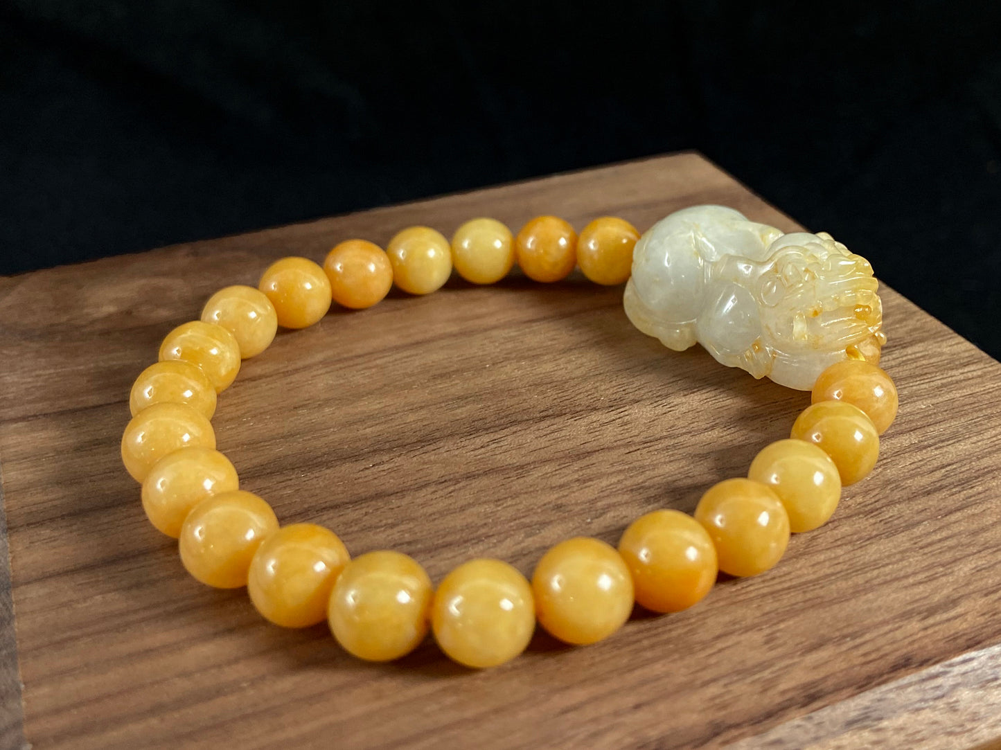 A jade bead strand featuring a white based gold flecked pixiu charm and yellow beads.