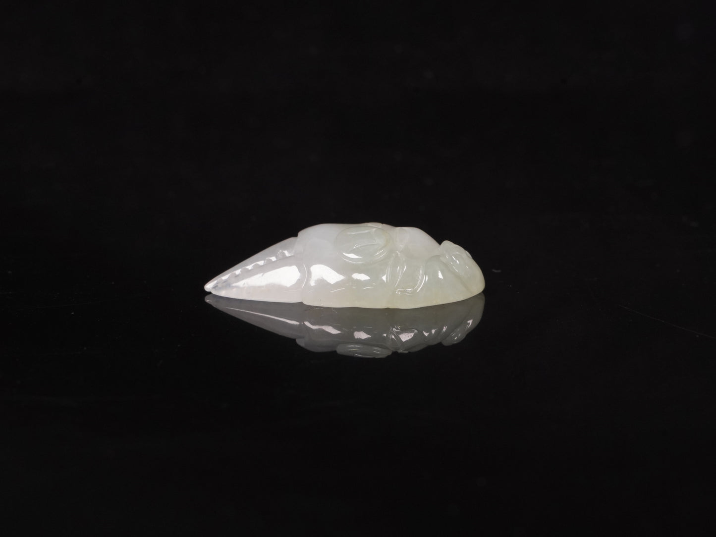 A crab-claw shaped jadeite piece with a milky white base and a subtle wash of pale green.