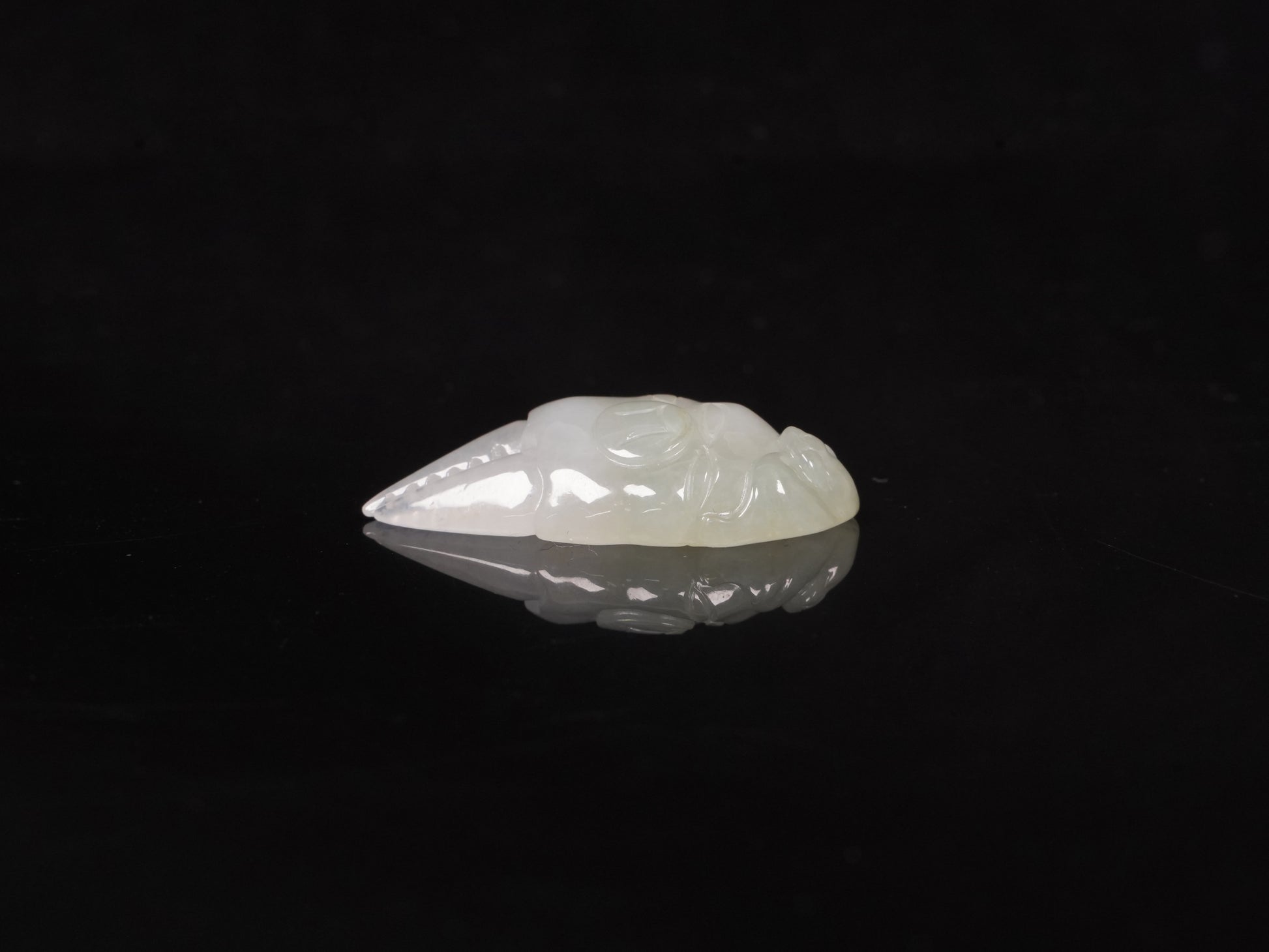 A crab-claw shaped jadeite piece with a milky white base and a subtle wash of pale green.