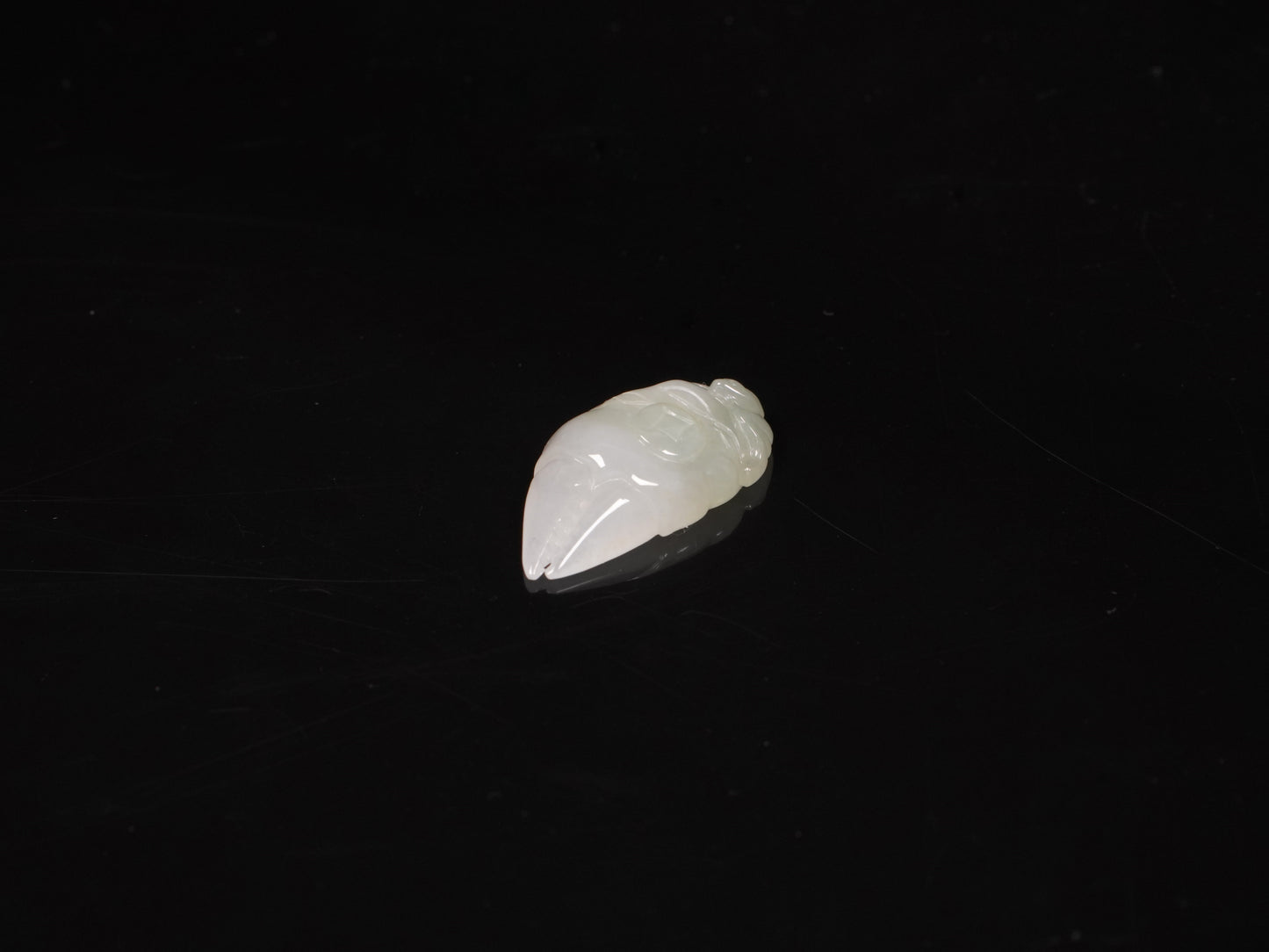 A crab-claw shaped jadeite piece with a milky white base and a subtle wash of pale green.