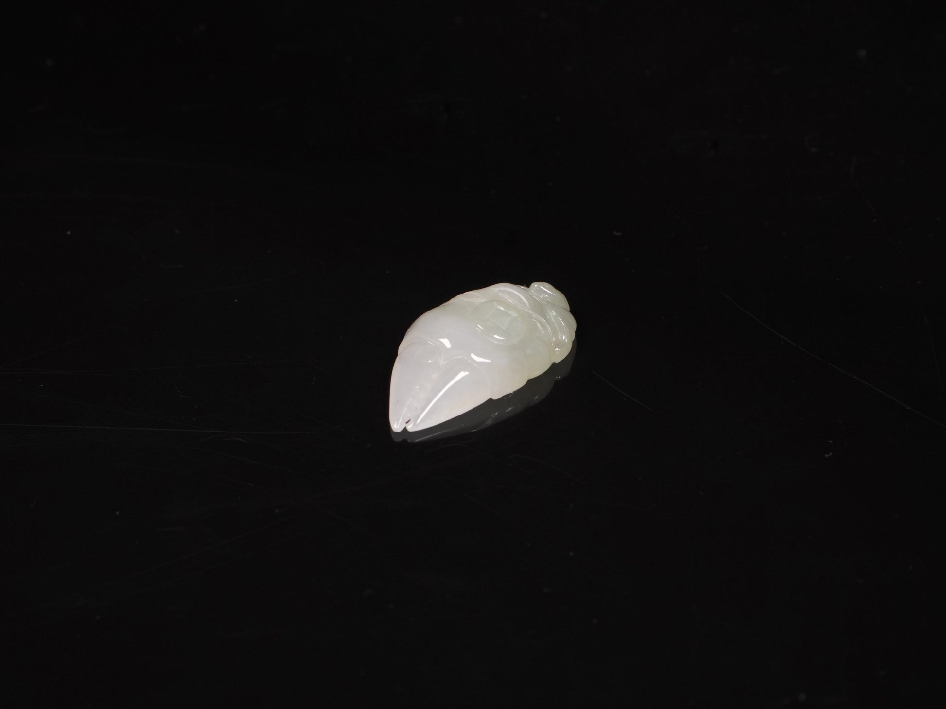 A crab-claw shaped jadeite piece with a milky white base and a subtle wash of pale green.