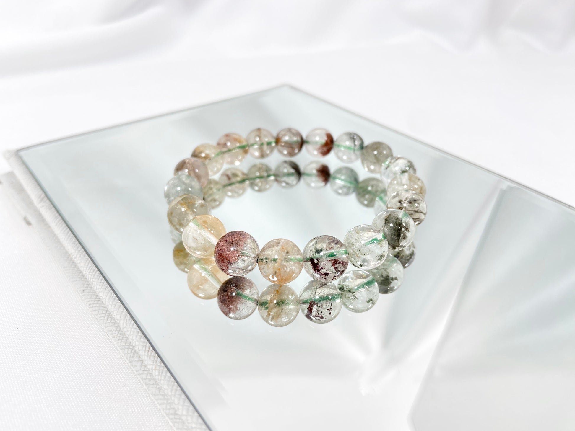 A phantom quartz bracelet showcasing white, red, golden, and pink inclusions.