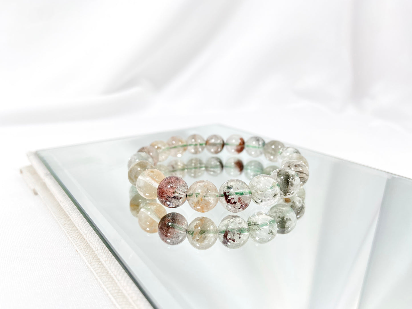 A phantom quartz bracelet showcasing white, red, golden, and pink inclusions.