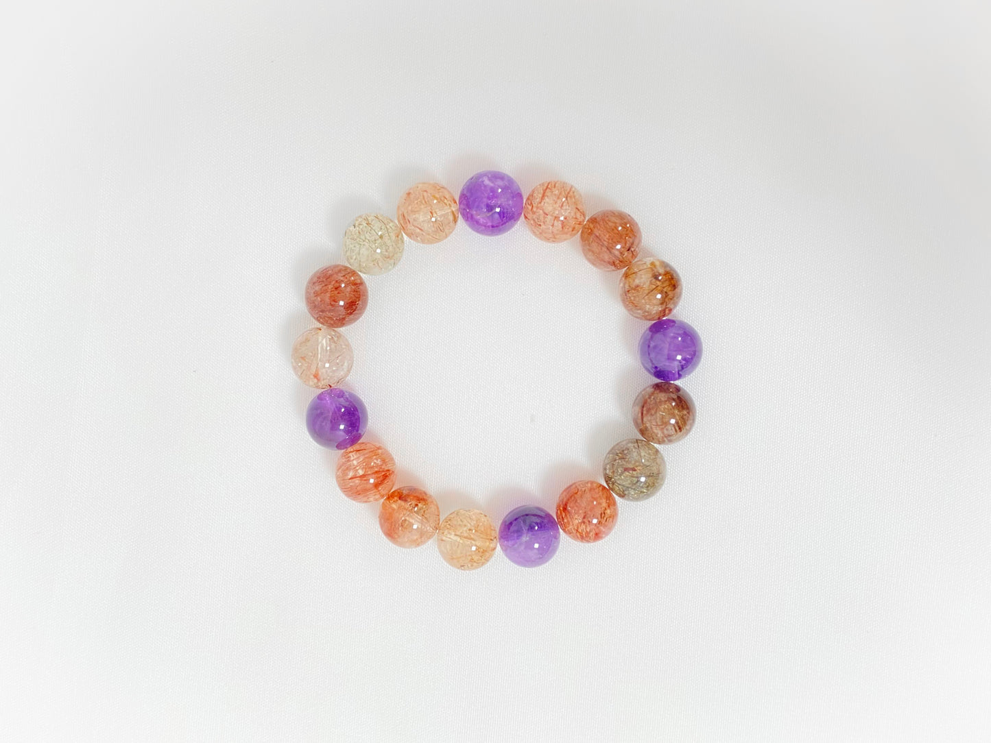 Super 7 crystal beads, a natural inclusion stone with hair-like, flaky, and speckled patterns in vibrant purple, red, orange, and black.