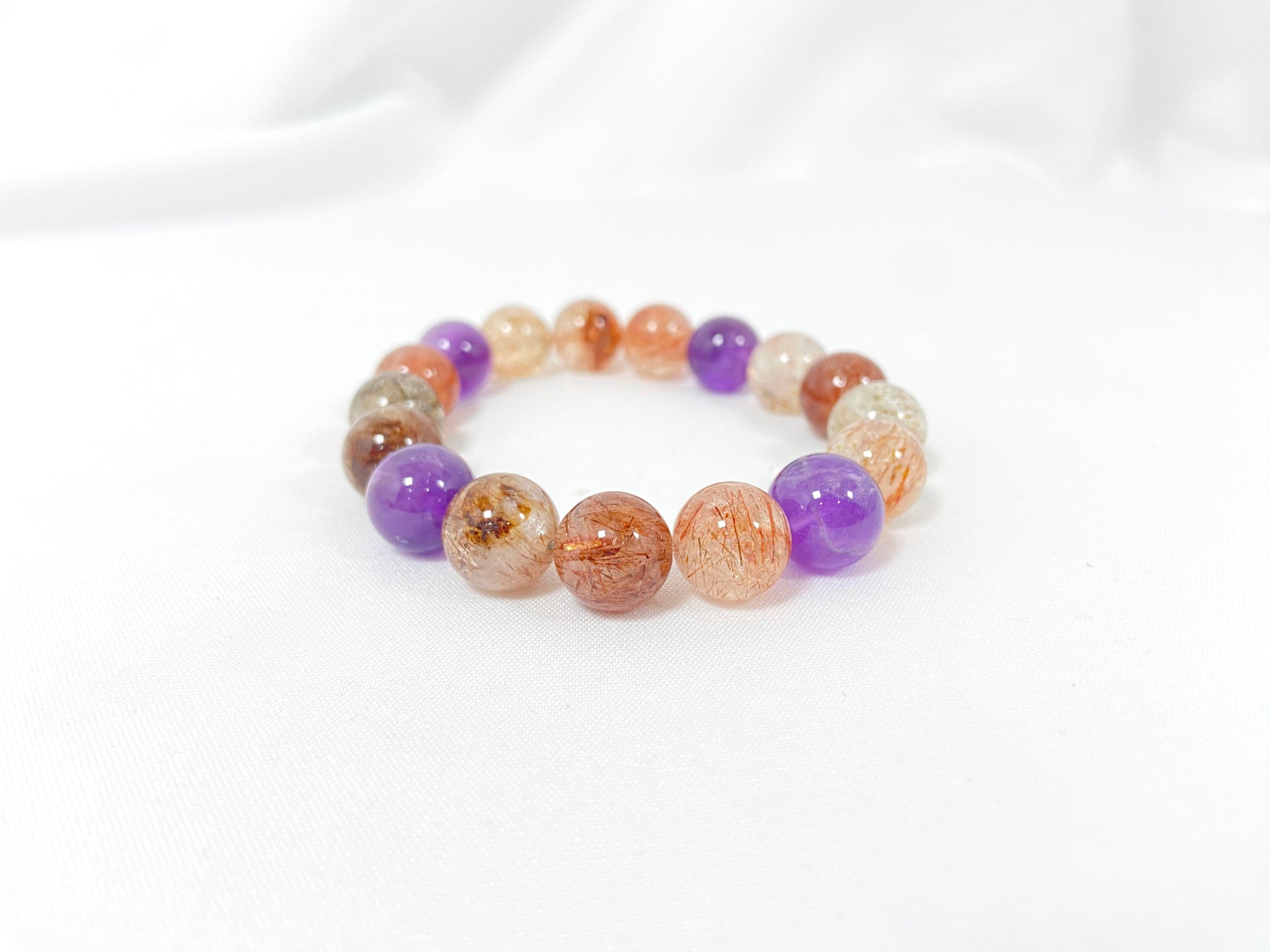 Super 7 crystal beads, a natural inclusion stone with hair-like, flaky, and speckled patterns in vibrant purple, red, orange, and black.