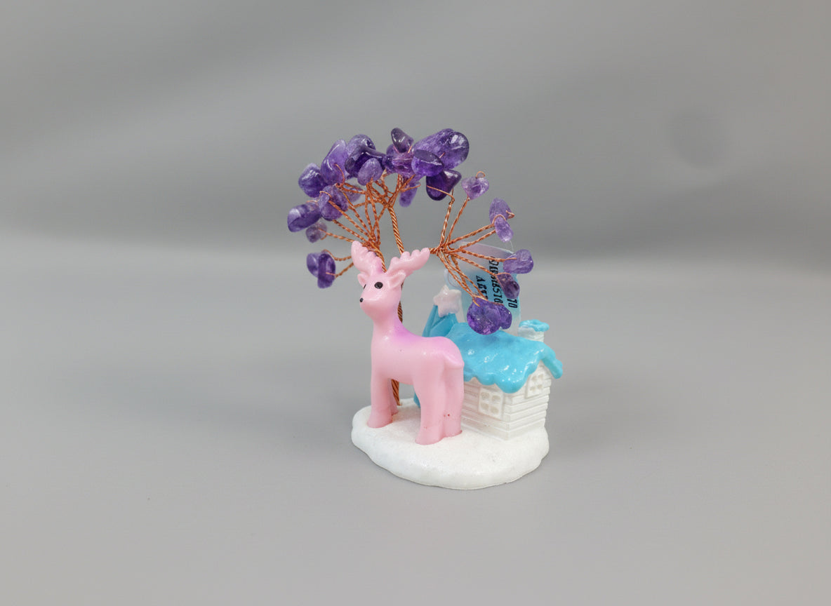 An amethyst crystal tree accompanied by a pink deer and a white cottage with a blue roof.