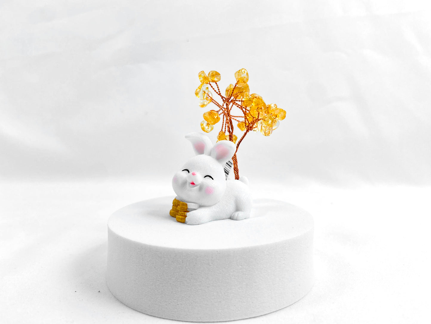 A citrine tree is set on a white rabbit holding several coins.