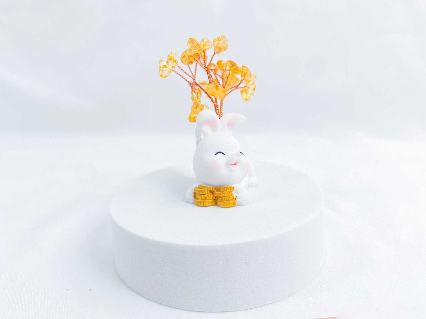 A citrine tree is set on a white rabbit holding several coins.