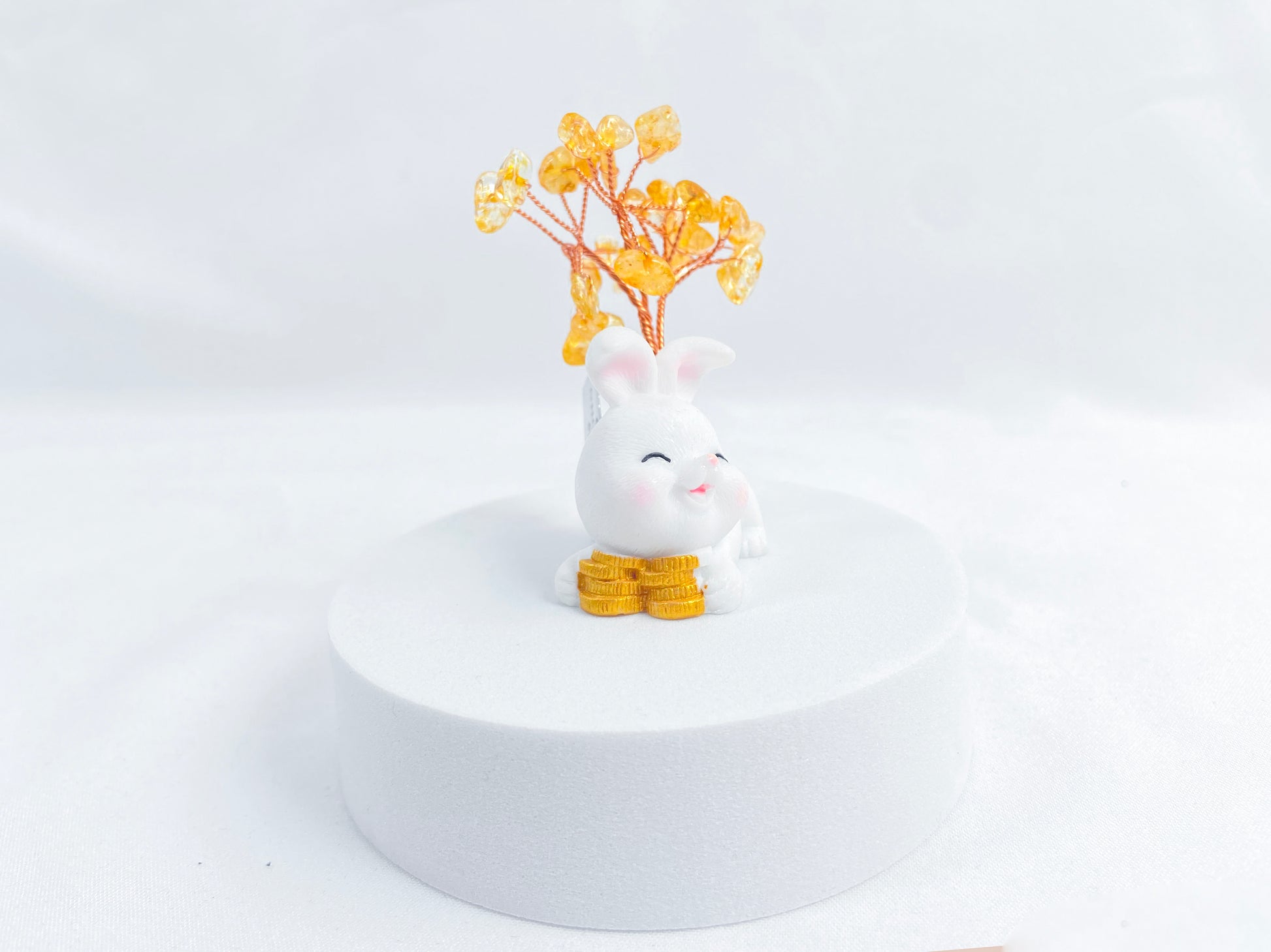 A citrine tree is set on a white rabbit holding several coins.
