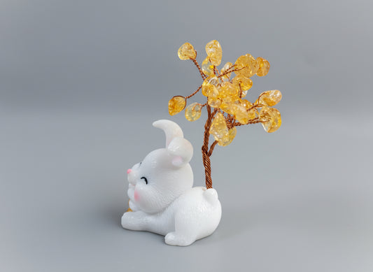A citrine tree is set on a white rabbit holding several coins.
