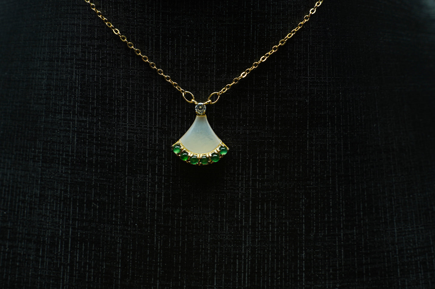 Gold necklace with a pendant featuring green gemstones on a black background