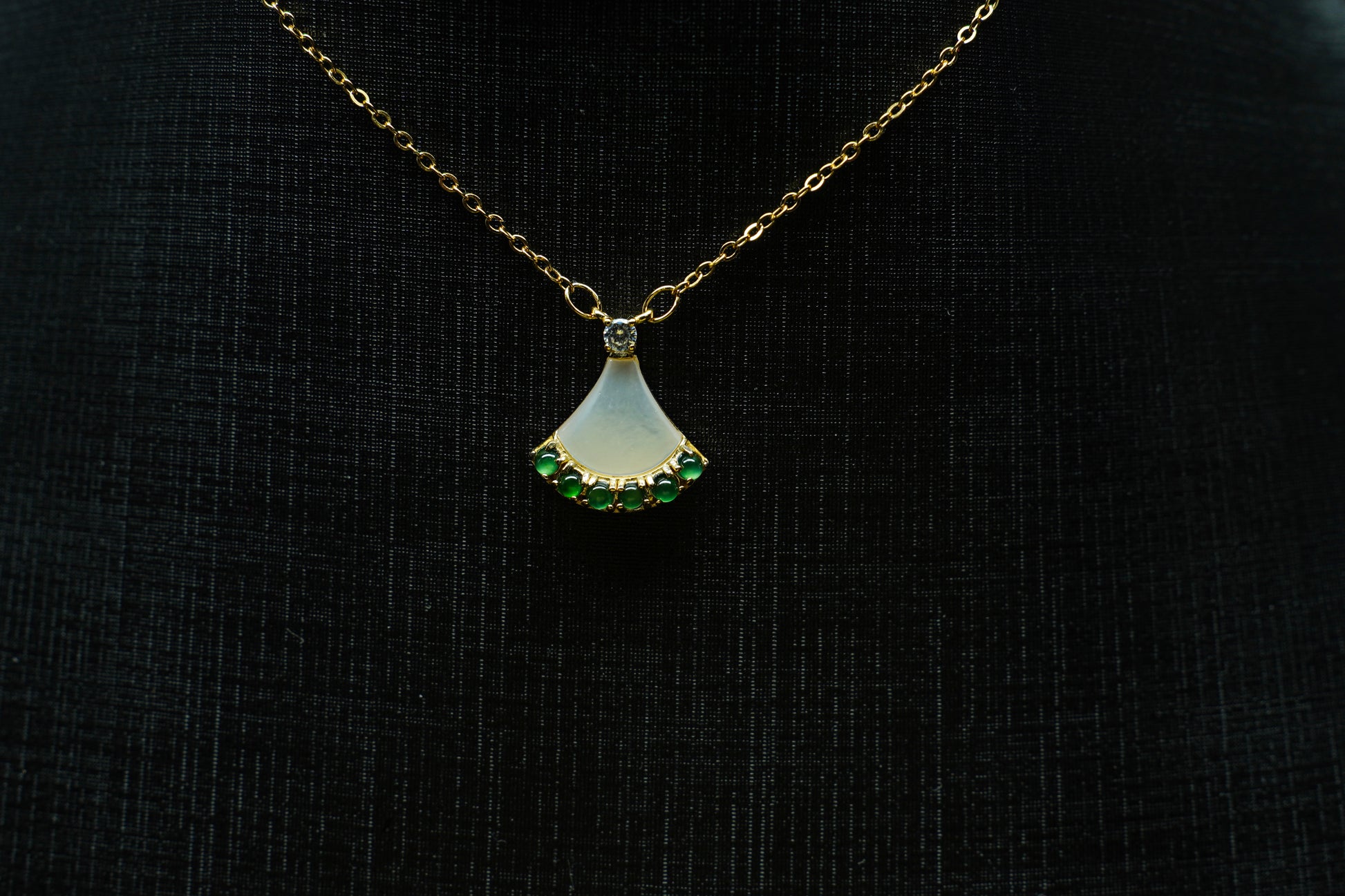 Gold necklace with a pendant featuring green gemstones on a black background