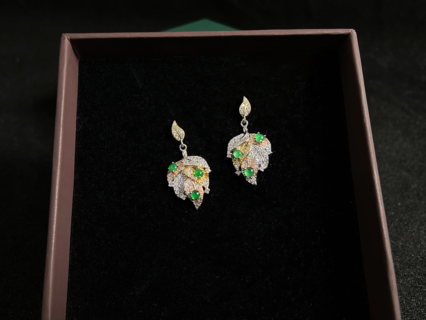 A pair of earrings featuring two 925 silver leaves, each adorned with three green jade beads, available in gold plated or natural silver finish.