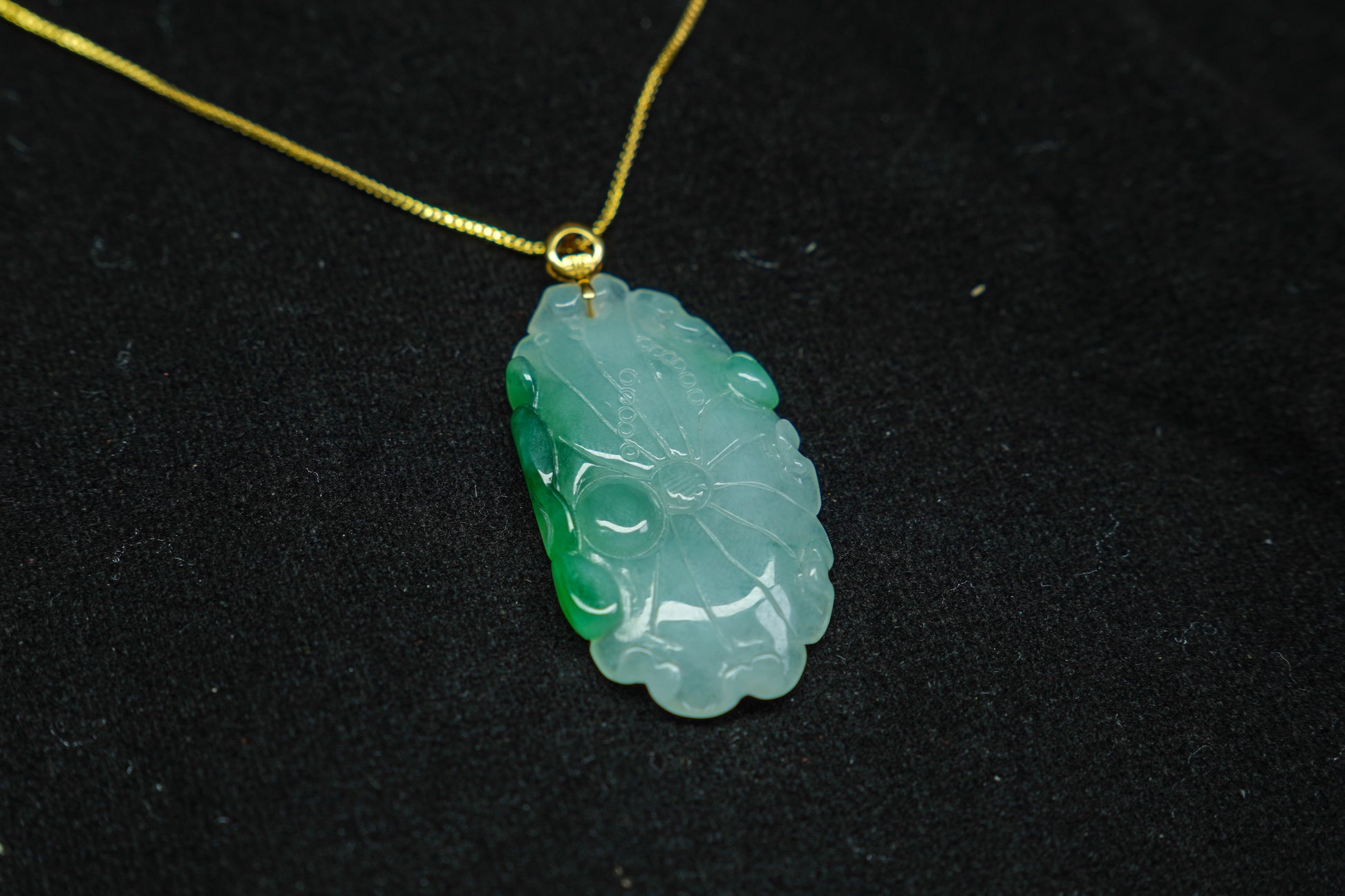 Green jade pendant on a gold chain against a black background
