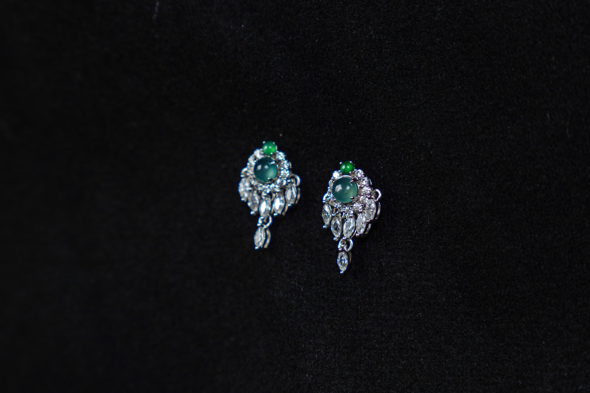Pair of silver earrings with green gemstones on a black background