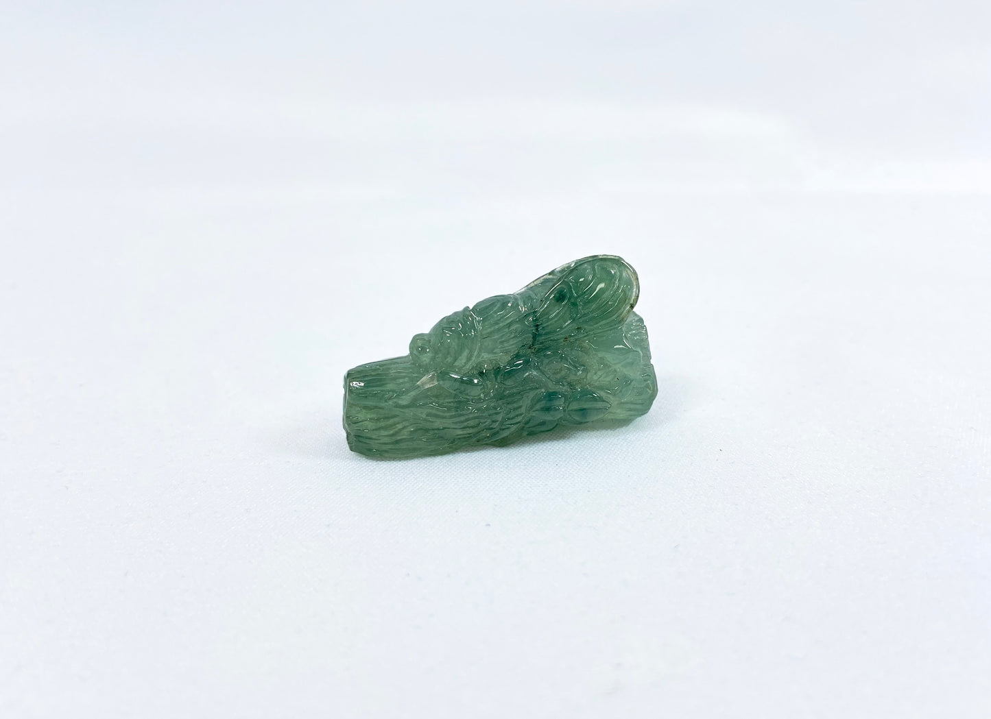 A transparent light green jadeite carved with a cicada on a tree trunk.