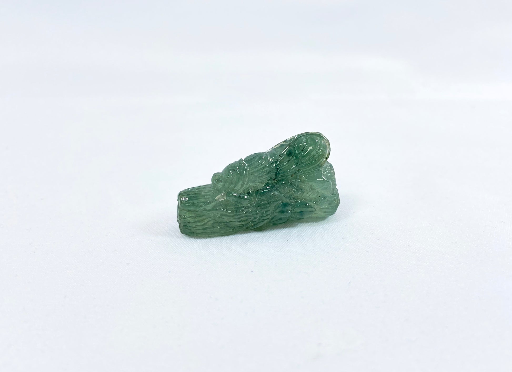 A transparent light green jadeite carved with a cicada on a tree trunk.