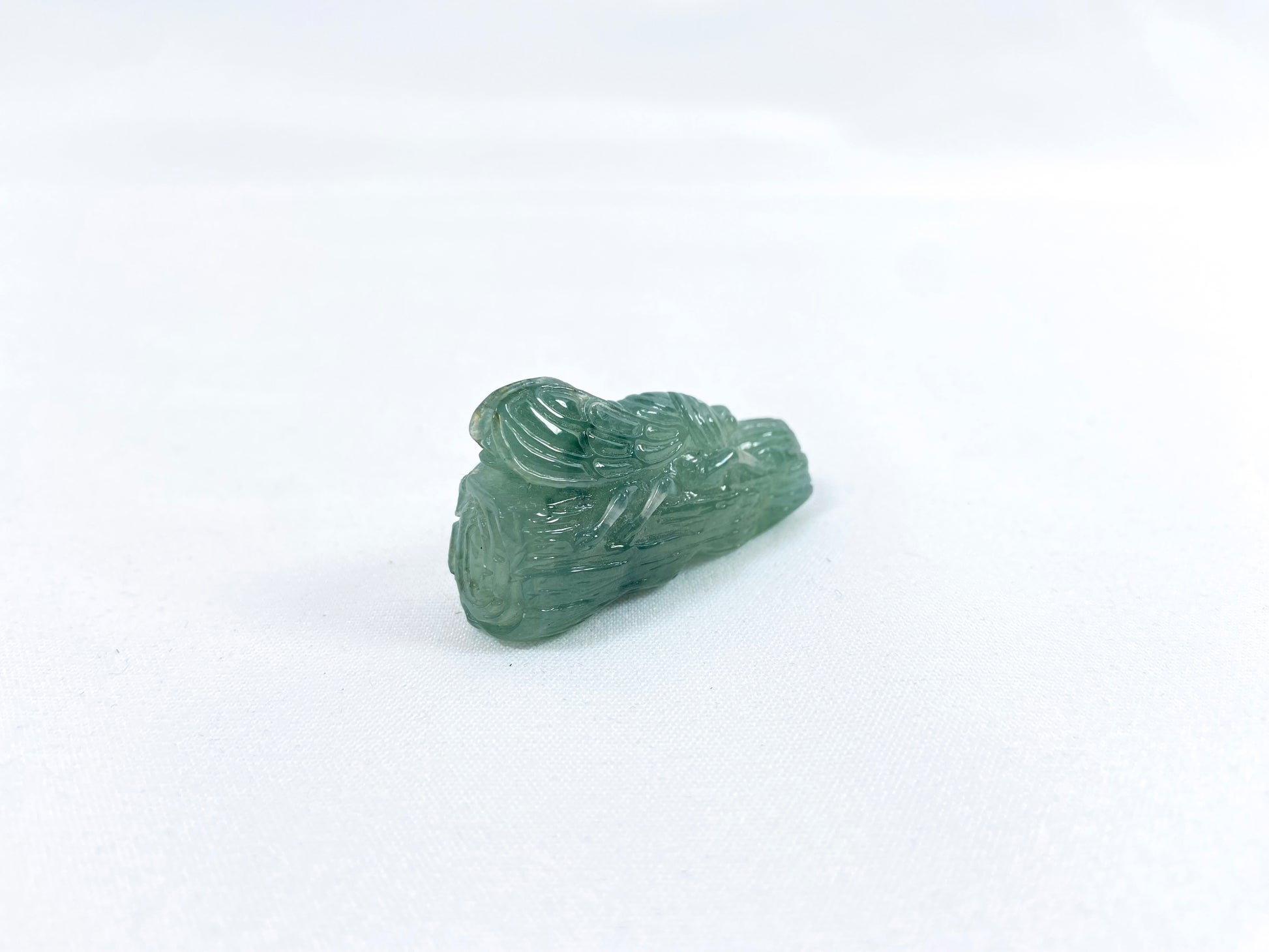 A transparent light green jadeite carved with a cicada on a tree trunk.