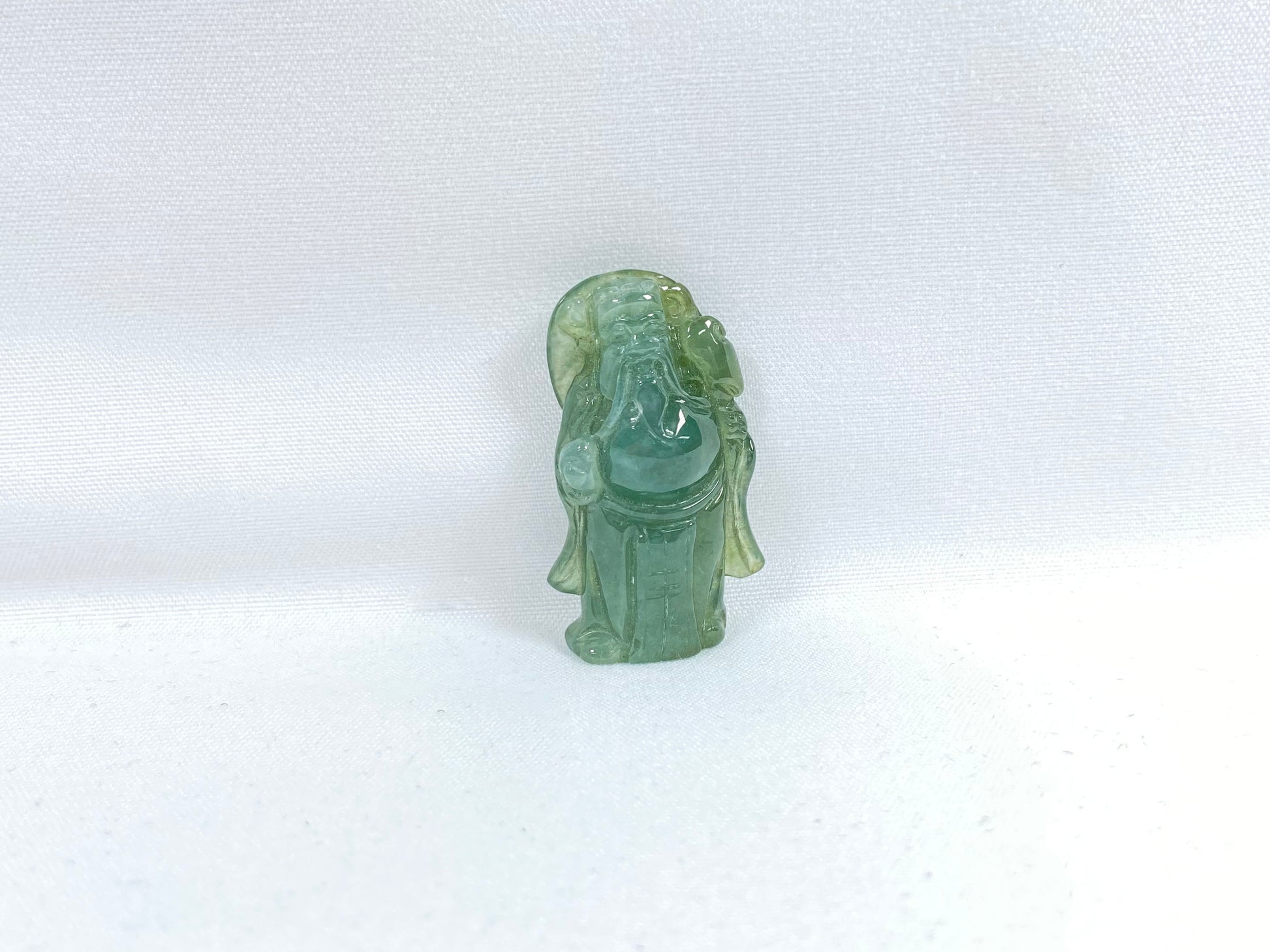 An icy light green jadeite loose stone carving of the God of Wealth.