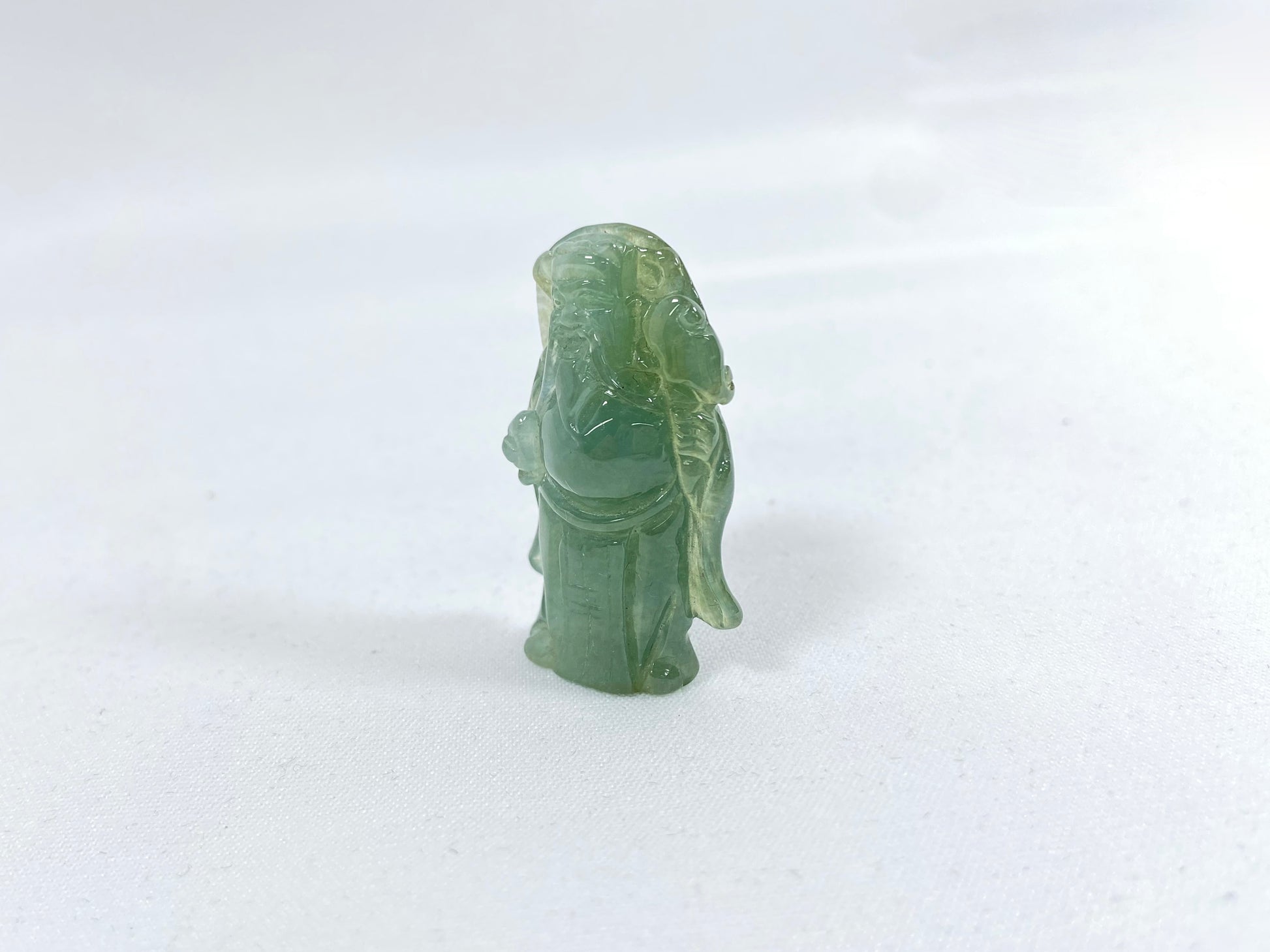 An icy light green jadeite loose stone carving of the God of Wealth.