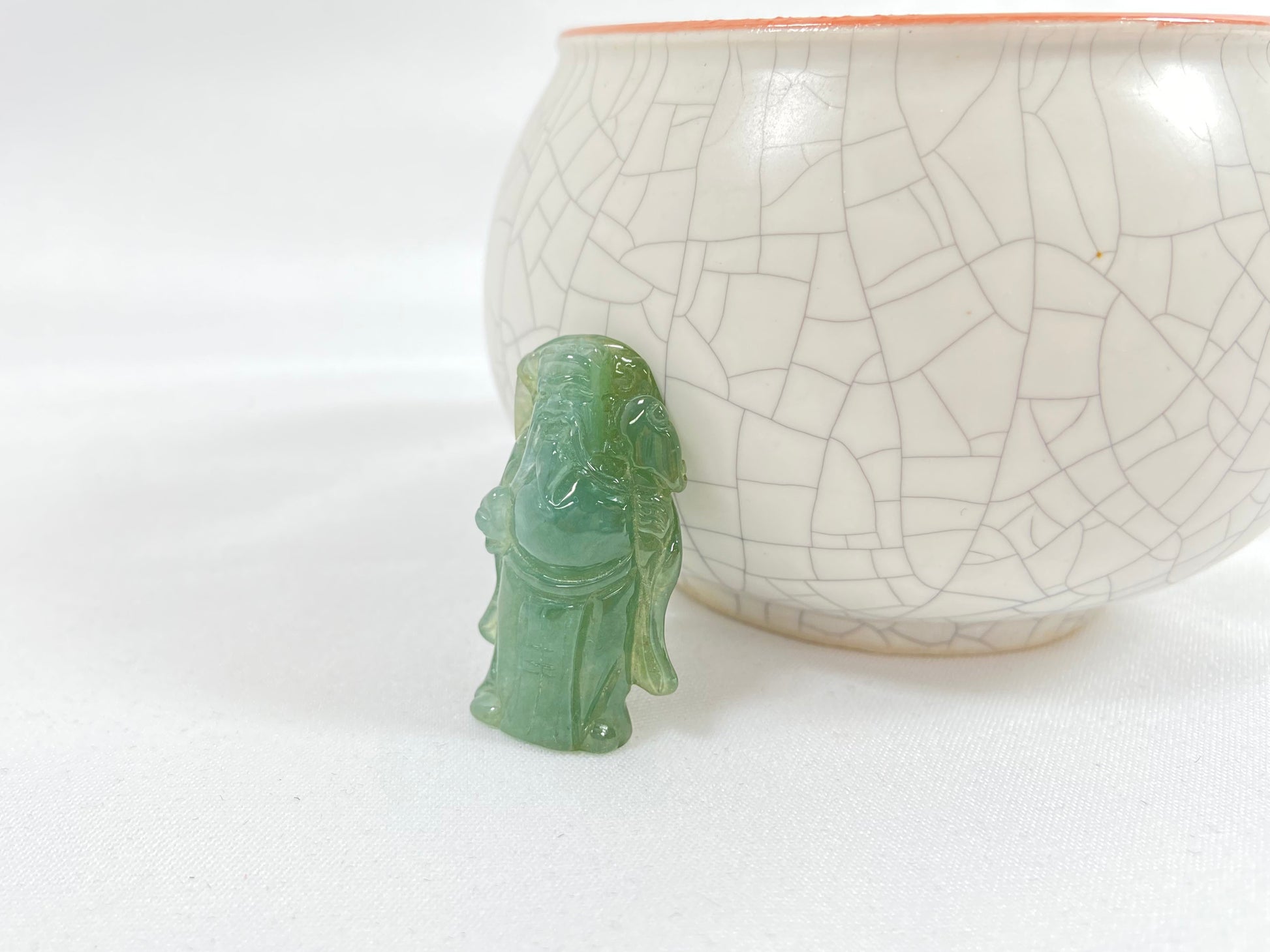 An icy light green jadeite loose stone carving of the God of Wealth.
