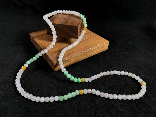 A jade bead strand featuring icy, white green, yellow, and brown beads with a golden focal bead.