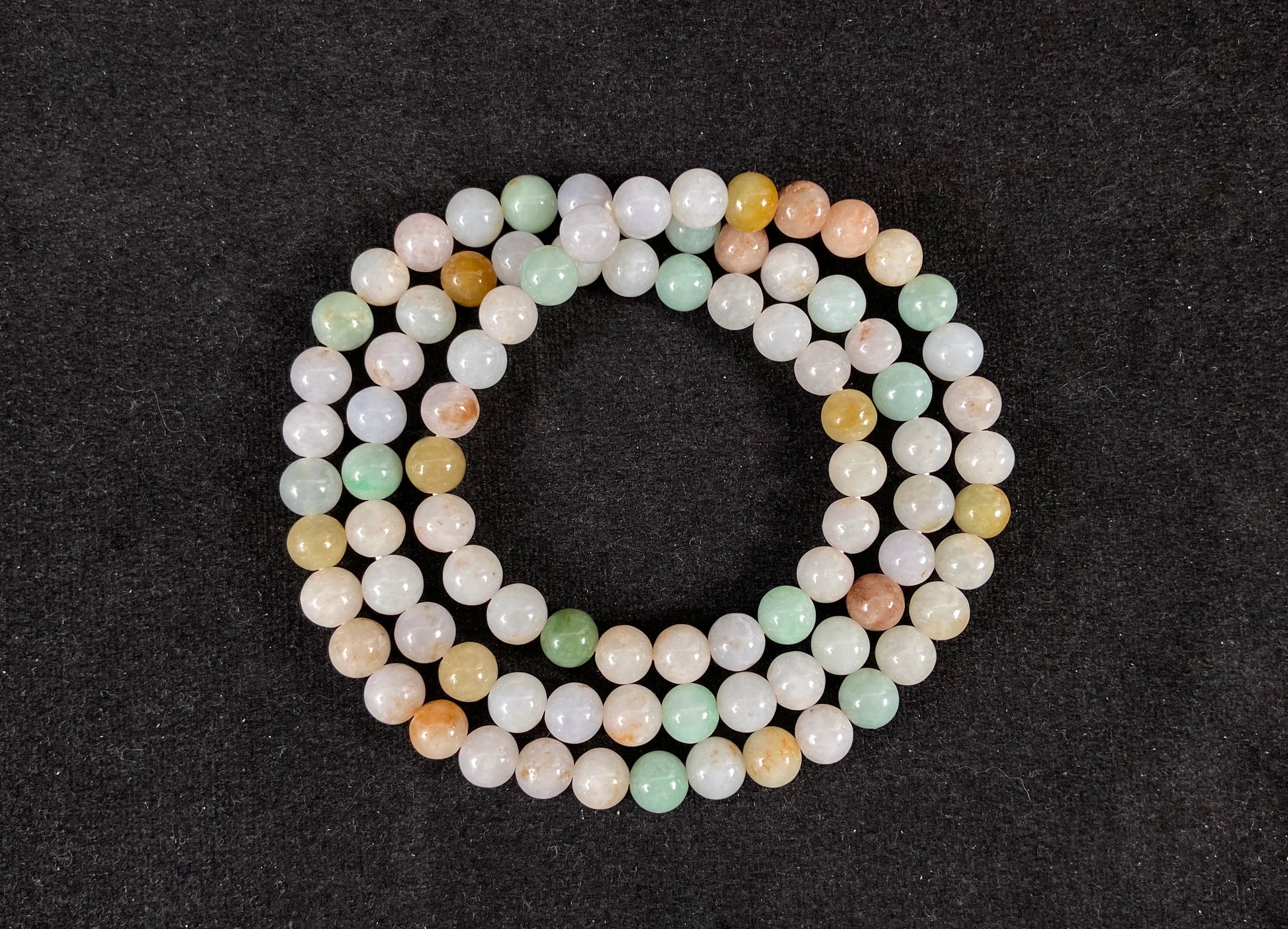 A jade bead strand featuring light green, tan, forest green, creamy white, and orange hues.