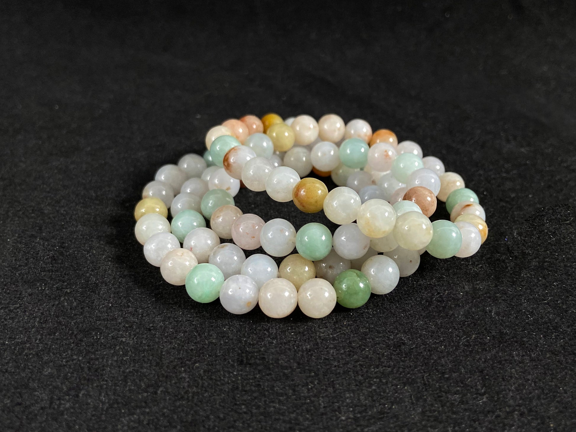 A jade bead strand featuring light green, tan, forest green, creamy white, and orange hues.