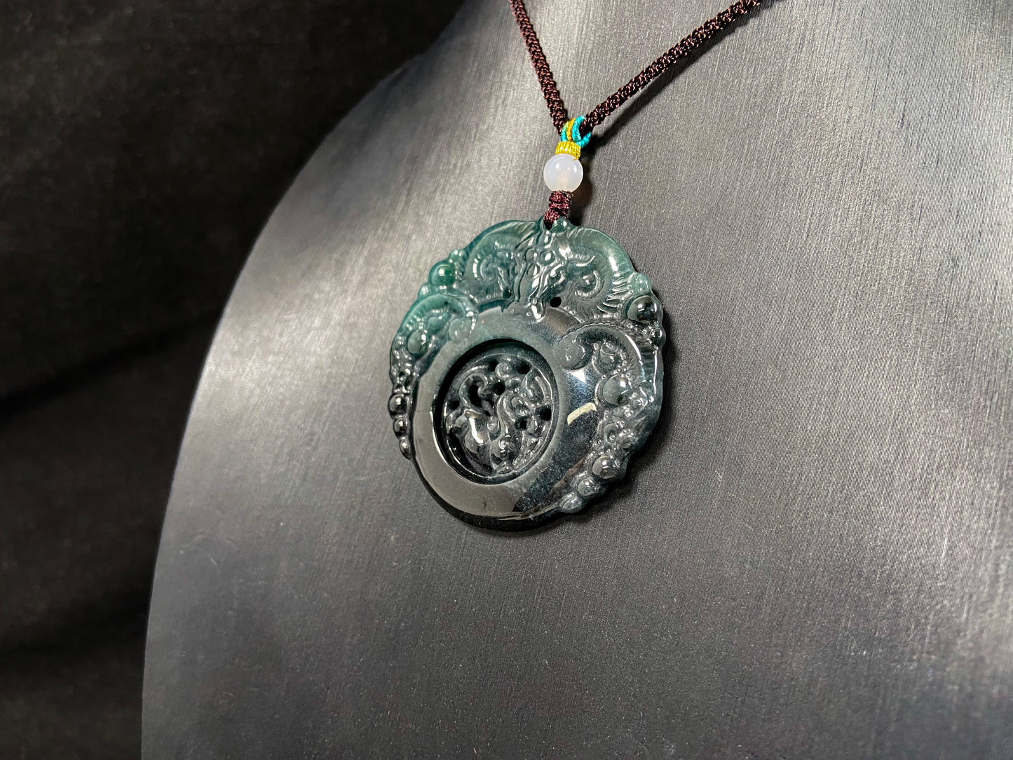 This jadeite pendant is a bi-color plaque, half deep green and half gray-black, carved with a kylin.