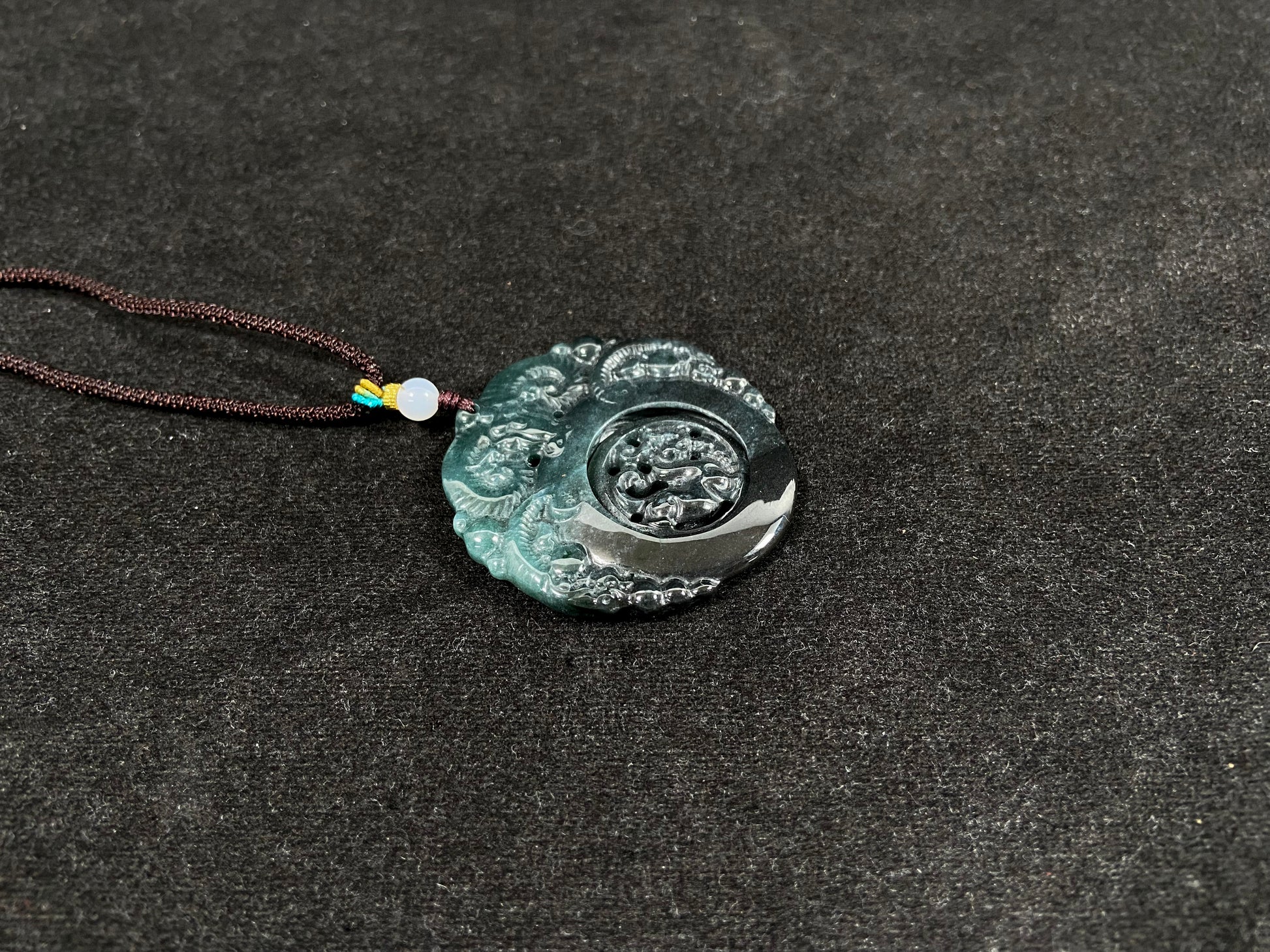 This jadeite pendant is a bi-color plaque, half deep green and half gray-black, carved with a kylin.