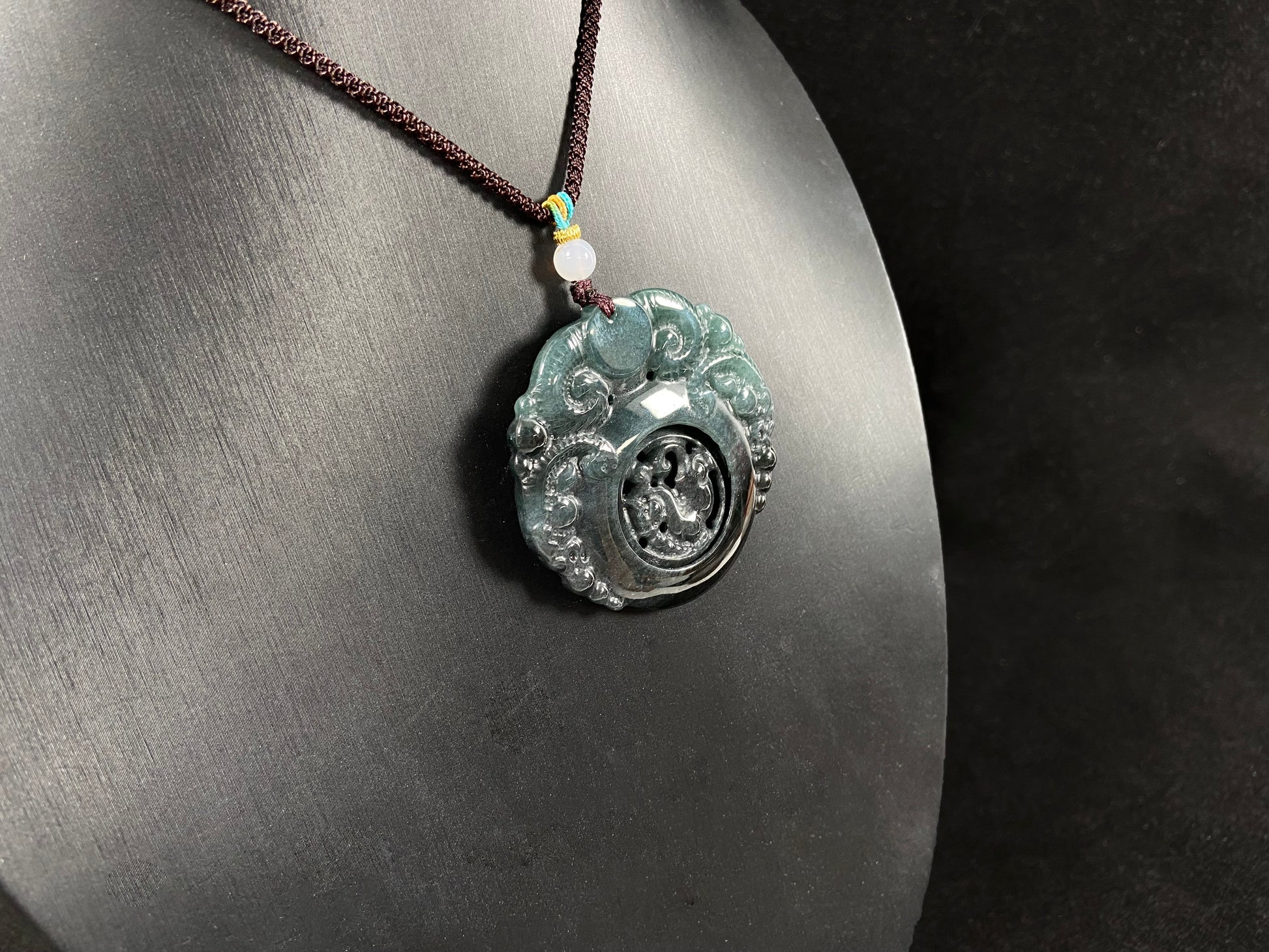 This jadeite pendant is a bi-color plaque, half deep green and half gray-black, carved with a kylin.
