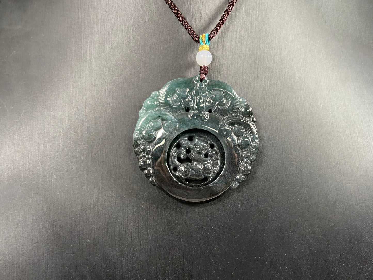 This jadeite pendant is a bi-color plaque, half deep green and half gray-black, carved with a kylin.