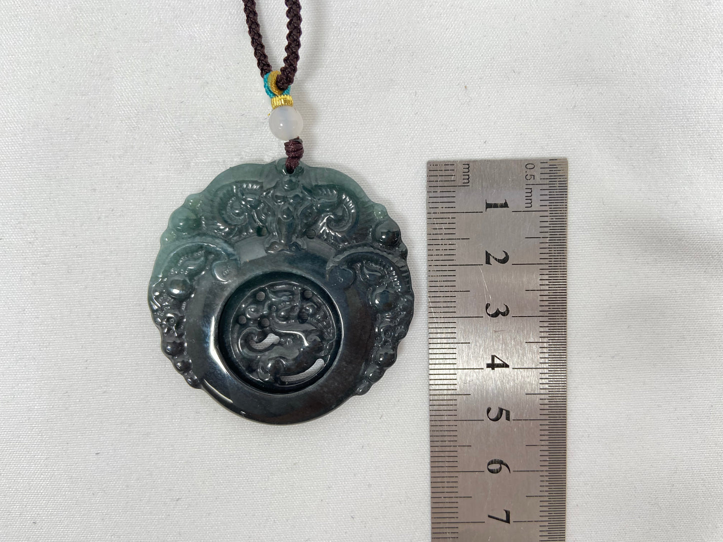 This jadeite pendant is a bi-color plaque, half deep green and half gray-black, carved with a kylin.