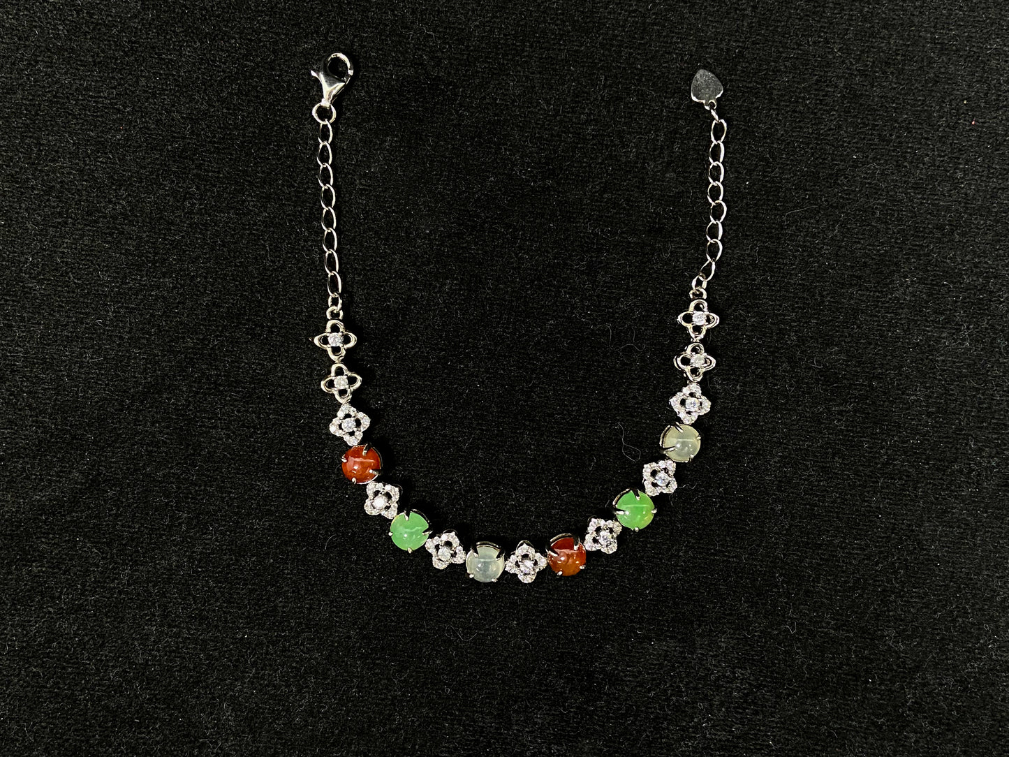 A jadeite bracelet with brown, green, and icy cabochons, each separated by sterling silver flowers set with diamond centers.